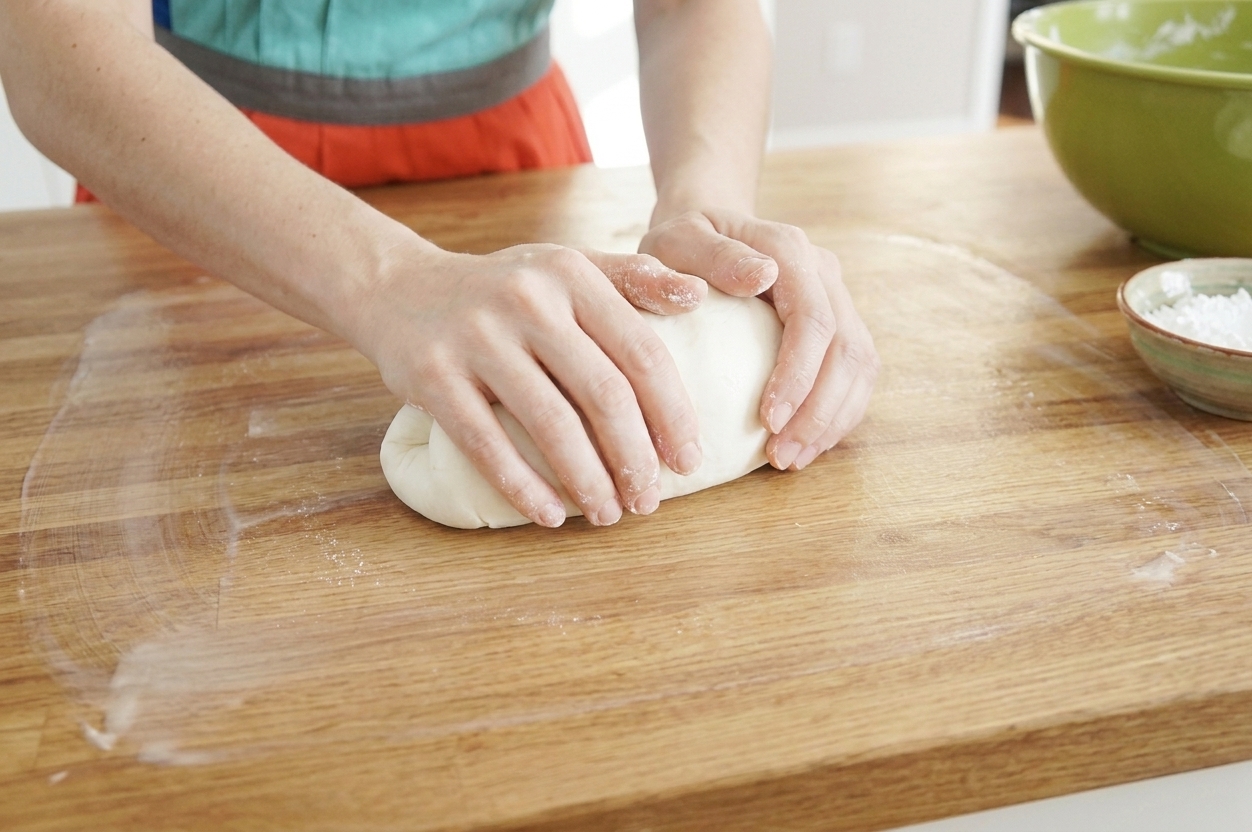 A pair of hands kneading a soft ball of fondant on a lightly greased kitchen counter