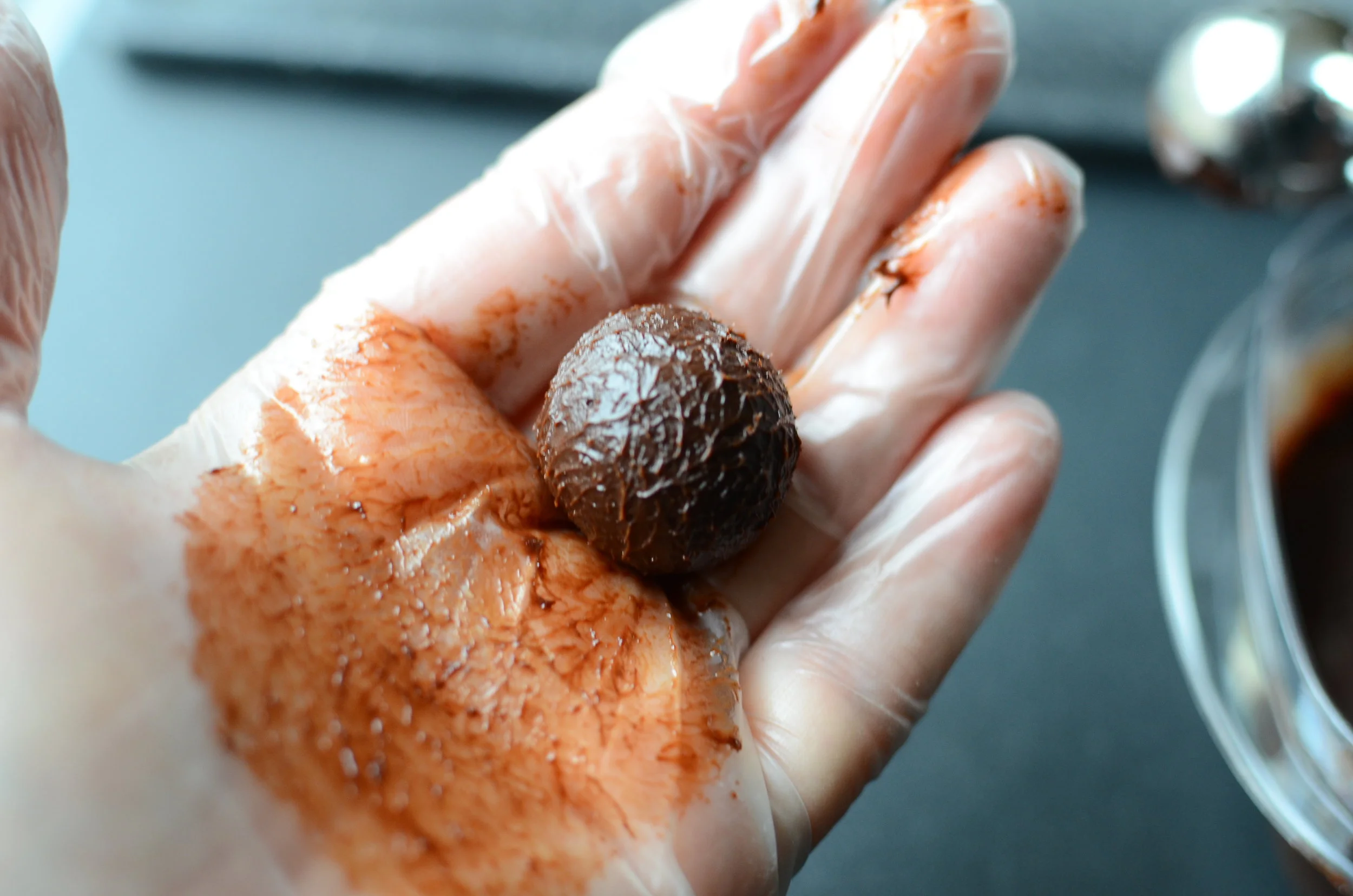 A pair of hands rolling a small ball of chocolate ganache over a parchment-lined sheet pan on a kitchen counter with warm lighting