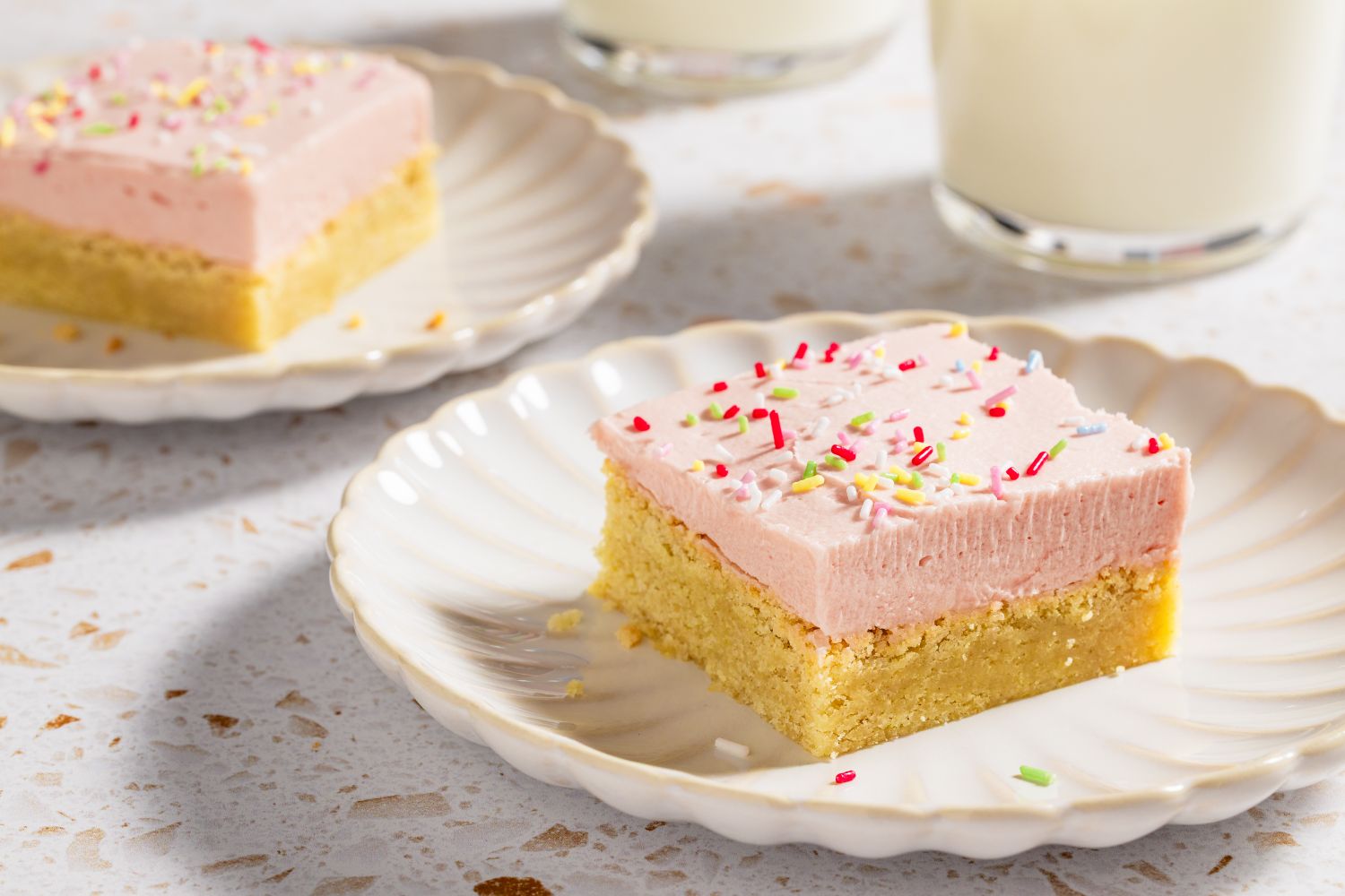 A pair of hands using an offset spatula to swirl cream cheese frosting over cookie bars in a baking pan on a bright kitchen counter