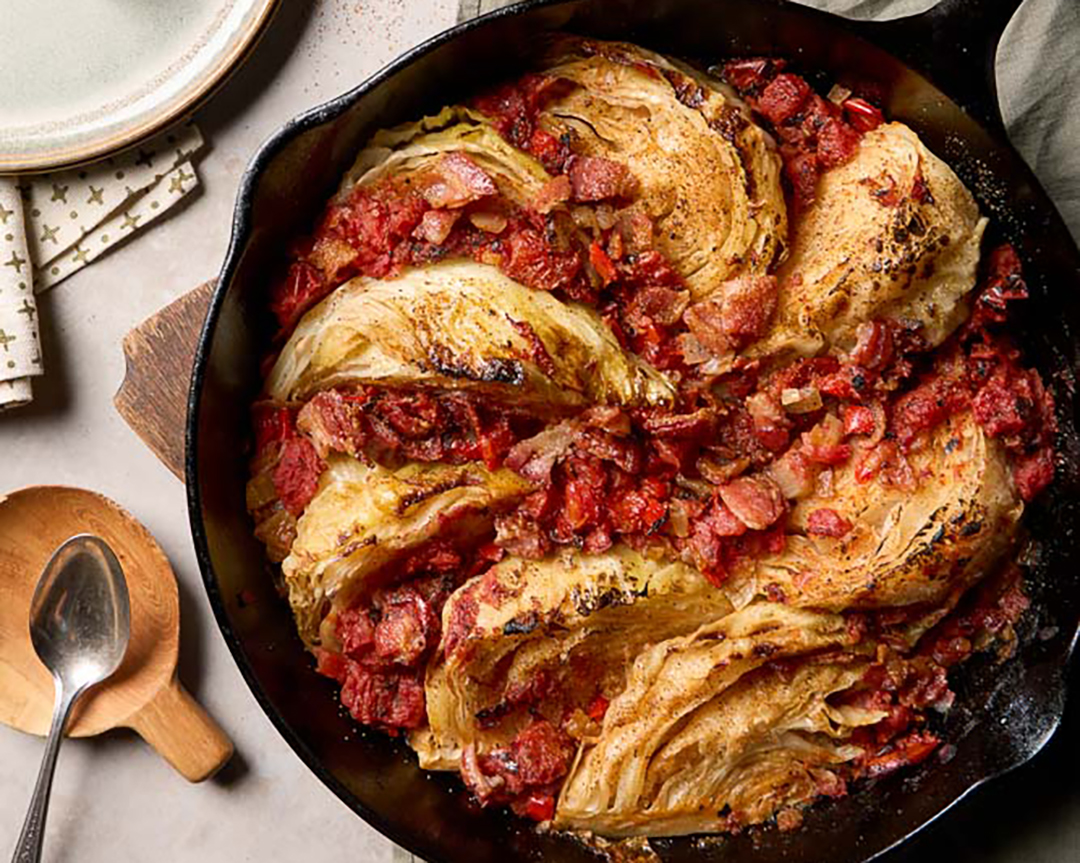A pan filled with glossy braised green cabbage, crispy bacon pieces, and caramelized onions with a bright, buttery finish