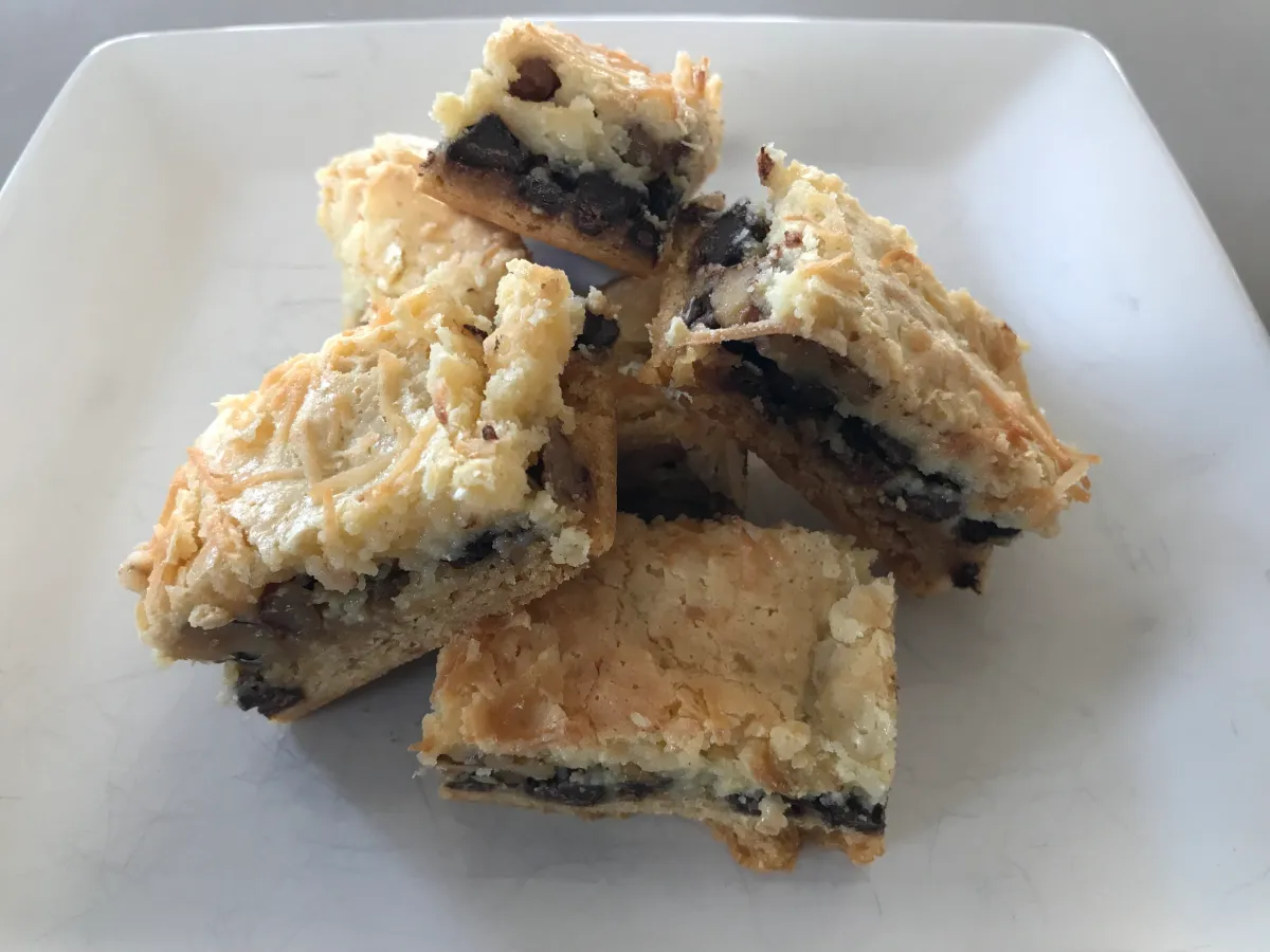 A pan of Neiman Marcus cake bars with golden edges and a soft cream cheese topping, cut into squares on a parchment-lined baking dish on a bright kitchen counter