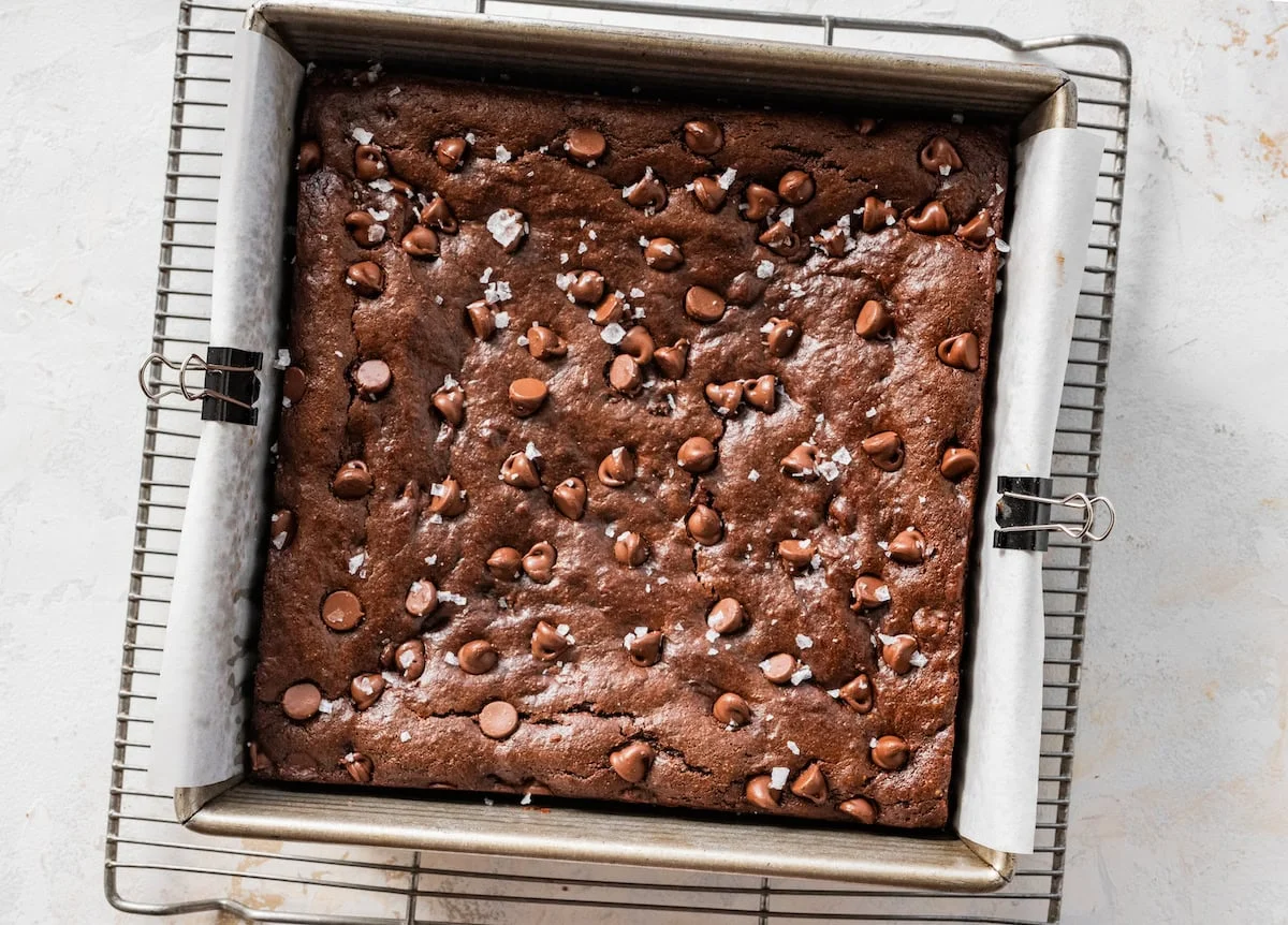 A pan of fudgy sweet potato brownies with crackly tops, cut into squares on a parchment-lined baking dish on a warm kitchen counter