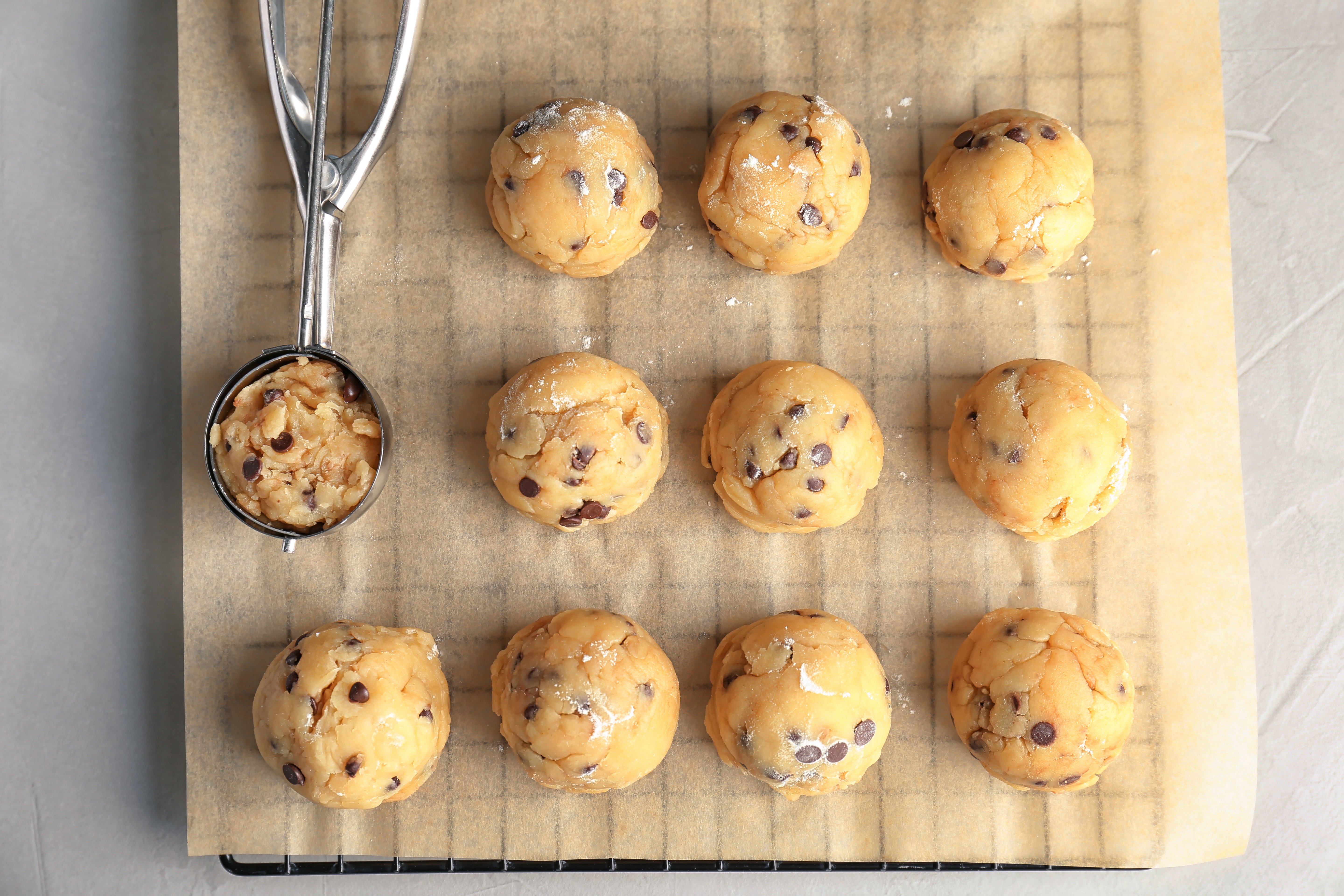 A parchment lined baking sheet in an oven with thick cookie dough balls spaced apart, just beginning to spread and turn golden at the edges