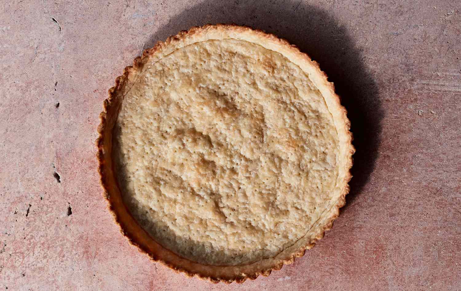 A partially baked pie crust in a glass pie dish on a baking sheet, lightly golden at the edges on a kitchen counter