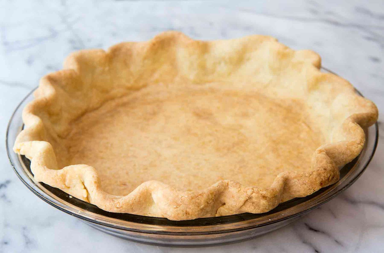 A partially baked pie crust in a glass pie dish on a baking sheet, parchment paper and pie weights visible