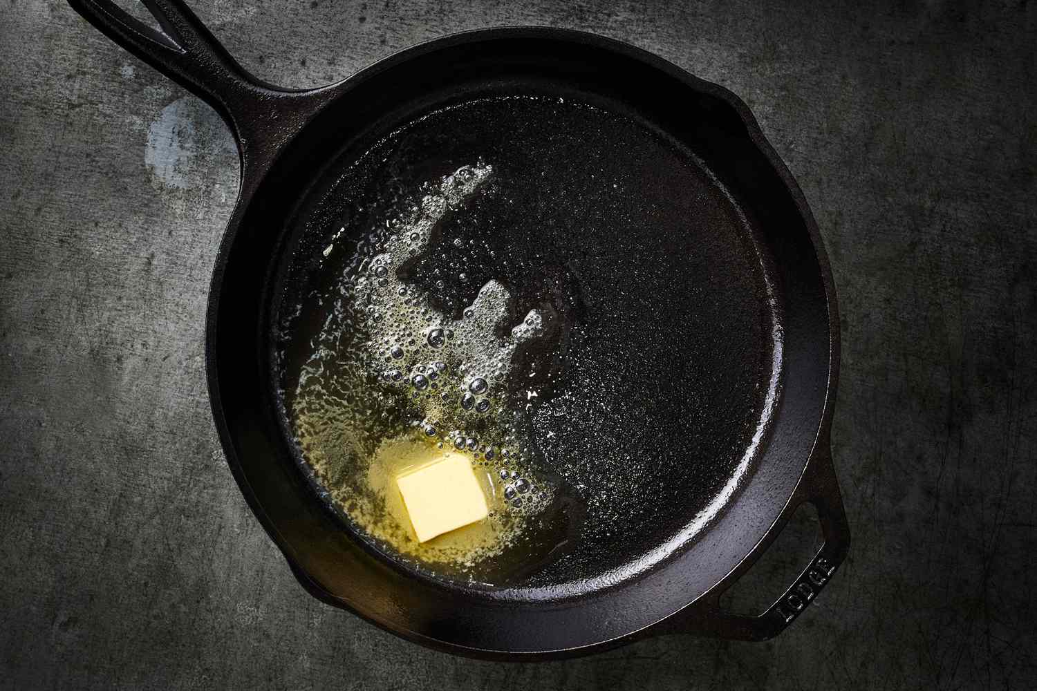 A pat of butter melting and sizzling in a preheated cast iron skillet on a stovetop, glossy and bubbling at the edges