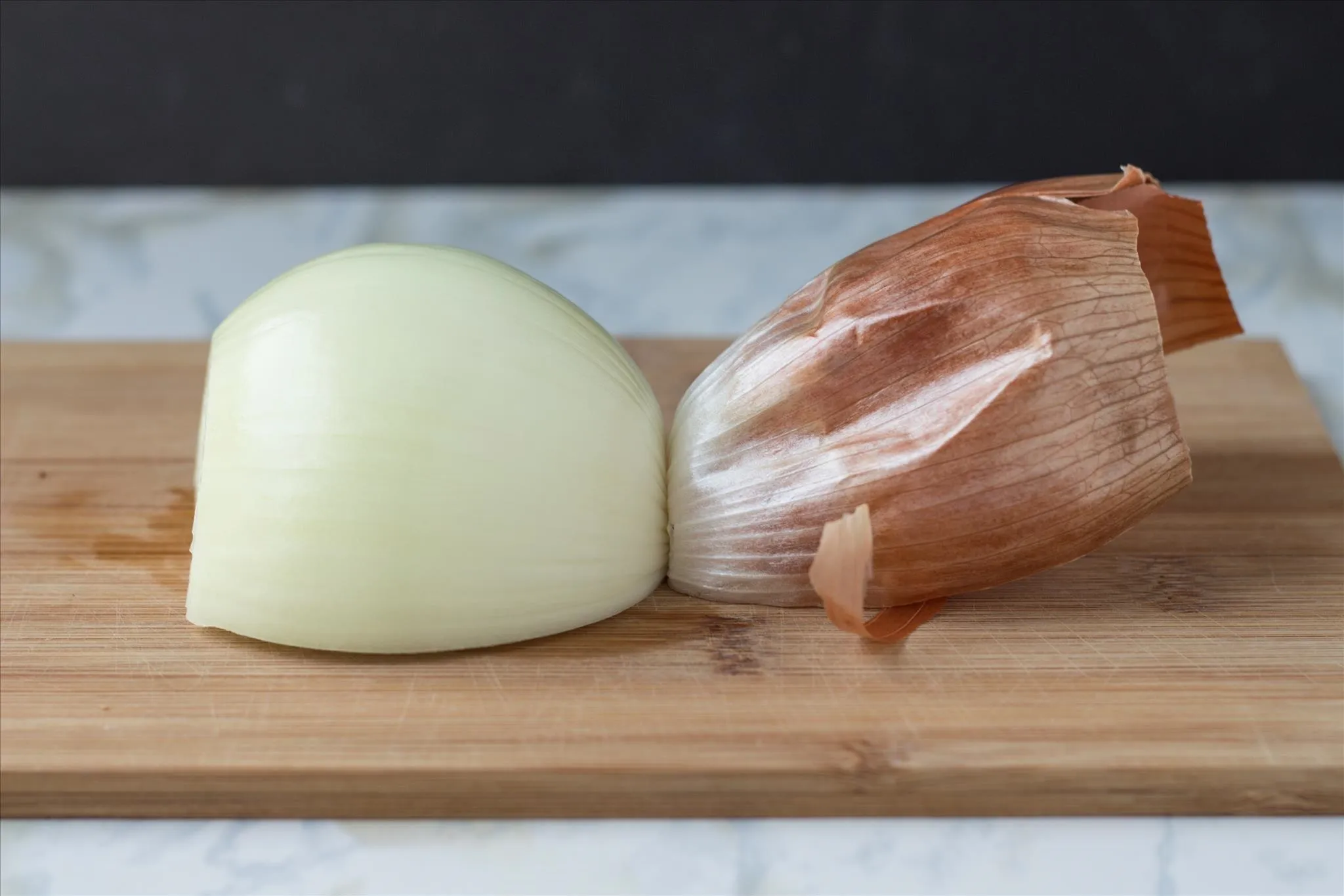 A peeled whole onion on a wooden cutting board with a chef’s knife nearby, ready to be cut for a foil packet recipe