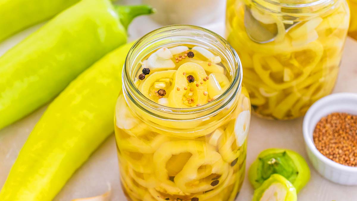 A pile of banana pepper rings and a few whole peppers on a cutting board in a home kitchen