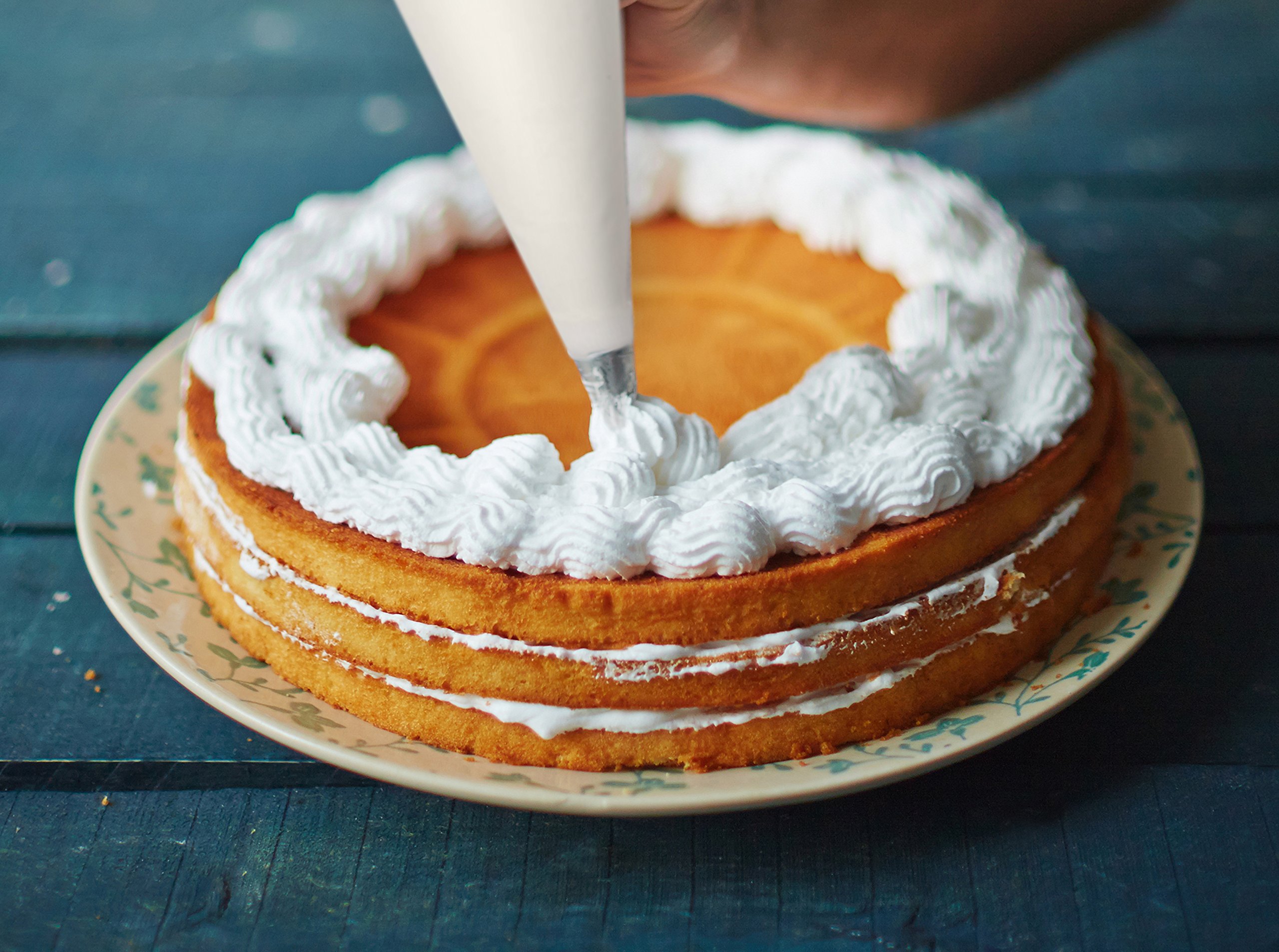 A piping bag fitted with a star tip filled with whipped frosting resting on a kitchen counter next to frosted cupcakes