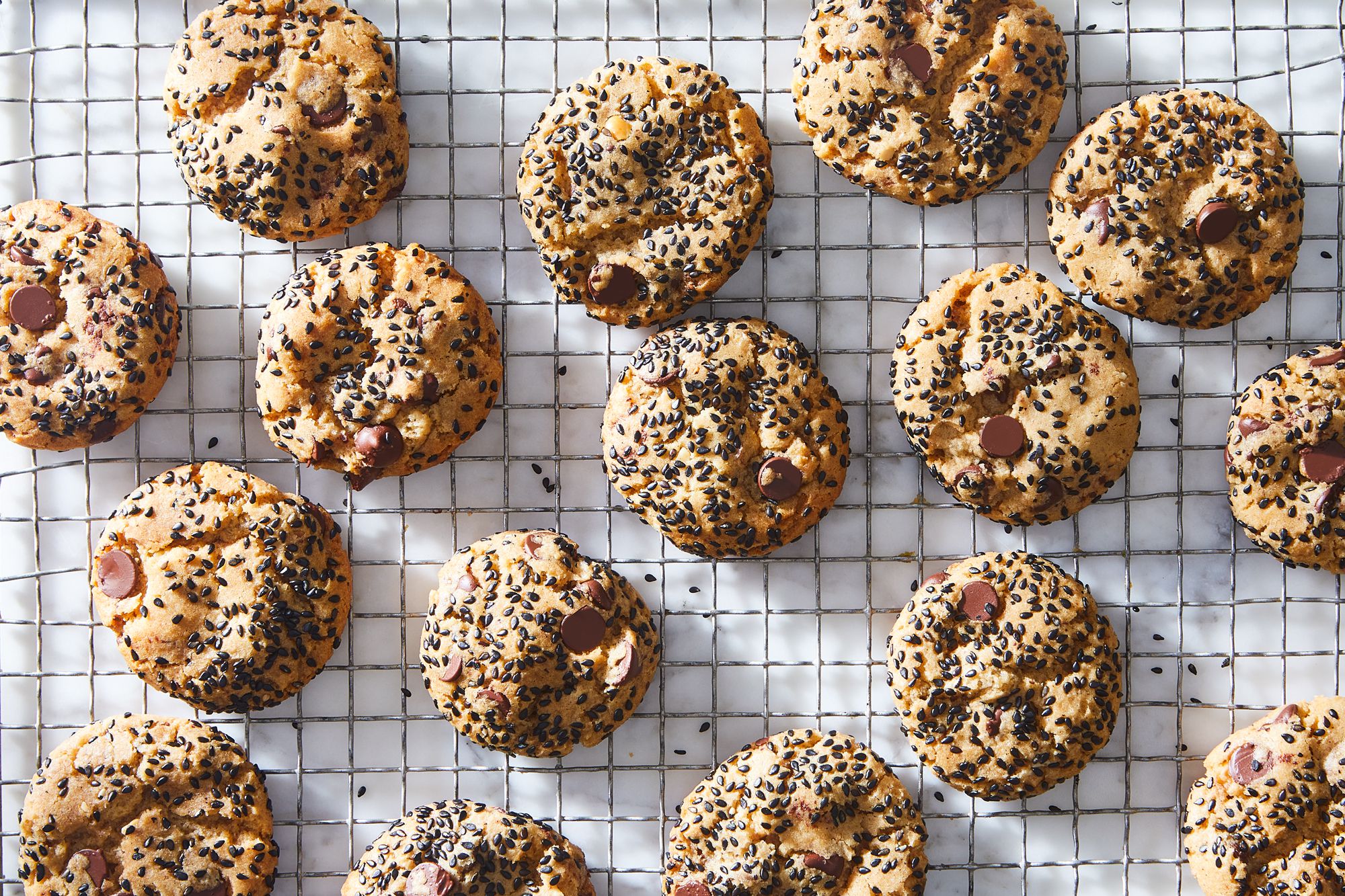 A plate of black sesame miso cookies with crackly tops and white chocolate chunks on a wooden kitchen table in warm natural light