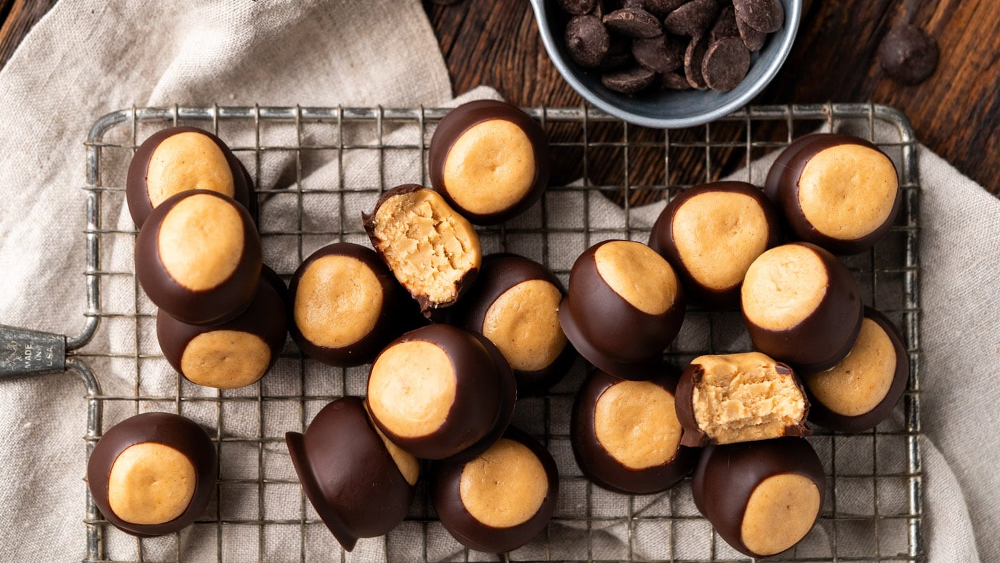 A plate of buckeye candies with glossy chocolate tops and a small circle of peanut butter showing, set on a warm kitchen table with soft natural light