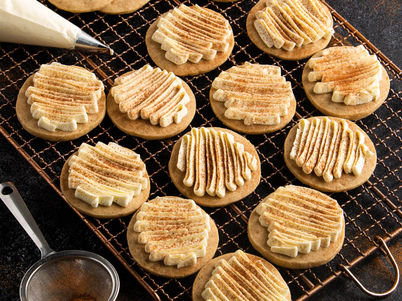 A plate of chai-spiced sugar cookies with vanilla glaze on a wooden kitchen table beside a mug of chai tea