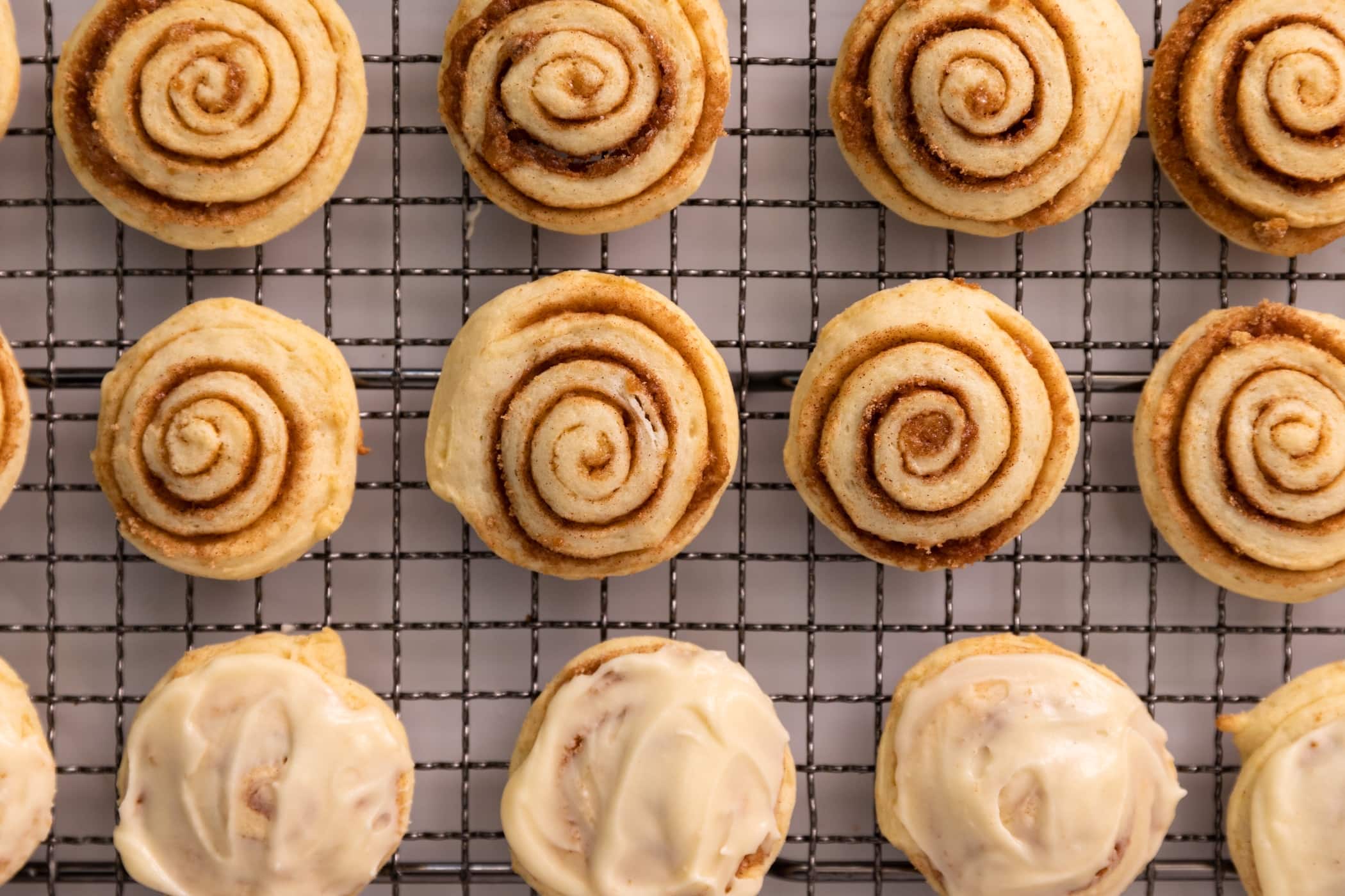 A plate of cinnamon roll cookies with visible cinnamon swirls and a light vanilla glaze, set on a warm-toned kitchen table with a linen napkin