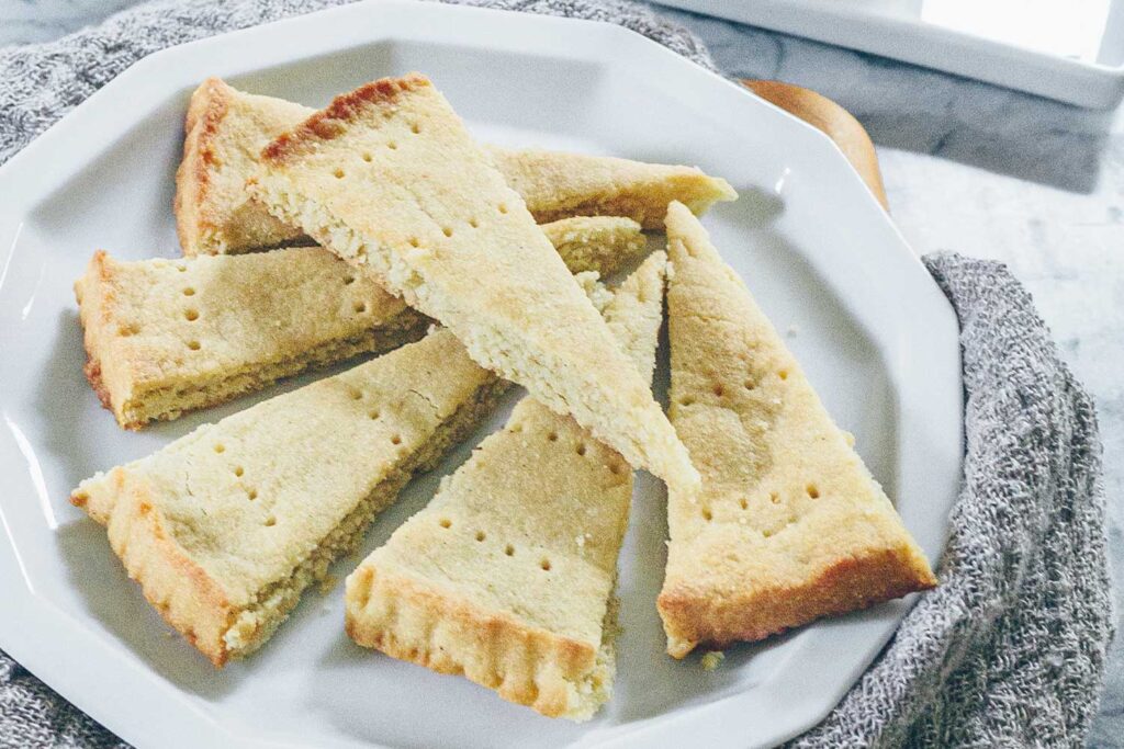 A plate of classic Scottish shortbread wedges with lightly golden edges on a linen napkin on a warm-toned kitchen table