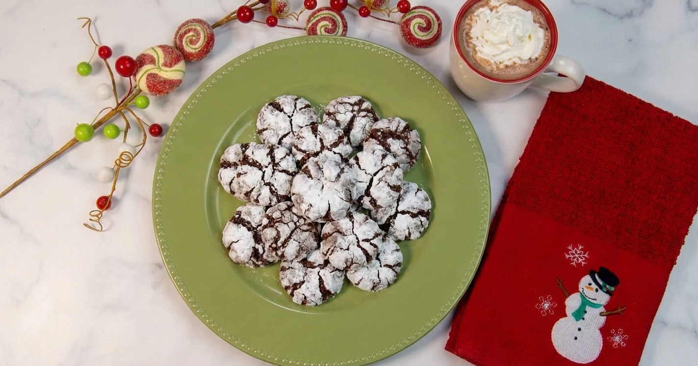 A plate of cooled chocolate crinkle cookies dusted with powdered sugar on a holiday table setting with a mug nearby