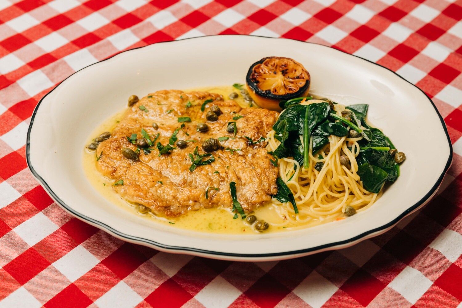 A plate of crispy breaded chicken cutlets topped with a glossy lemon-caper pan sauce, finished with parsley and lemon wedges on a warmly lit kitchen table