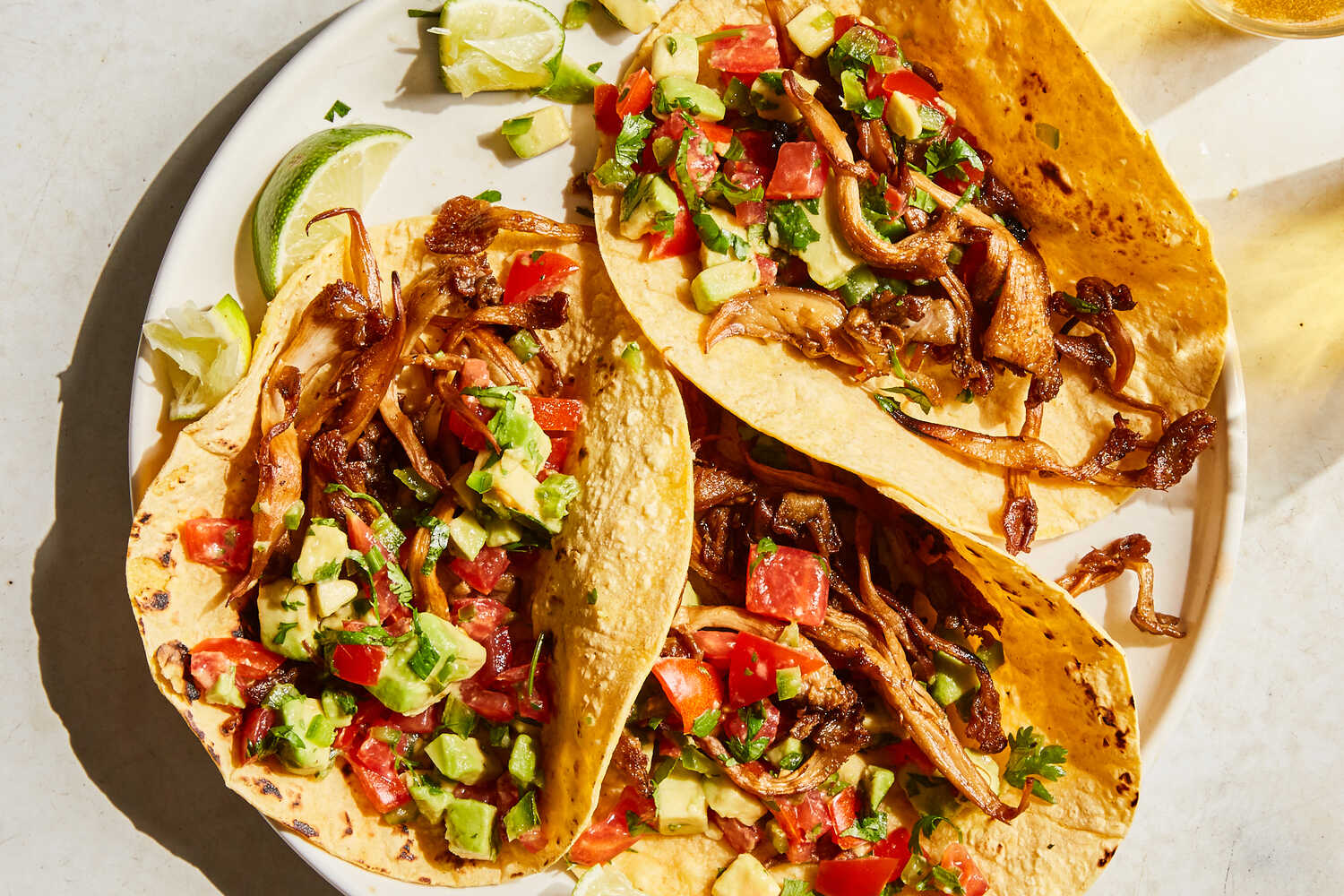 A plate of crispy oyster mushroom tacos topped with a crunchy cabbage slaw and drizzled with a smoky sauce on a warm, neutral-toned kitchen table