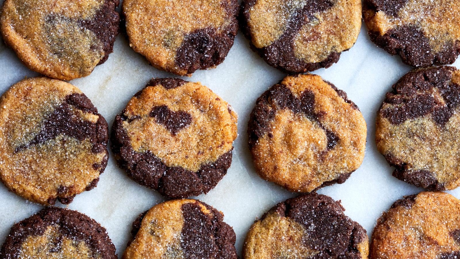 A plate of dark chocolate cookies with a visible cocoa swirl on top, set on a warm kitchen table with soft natural light
