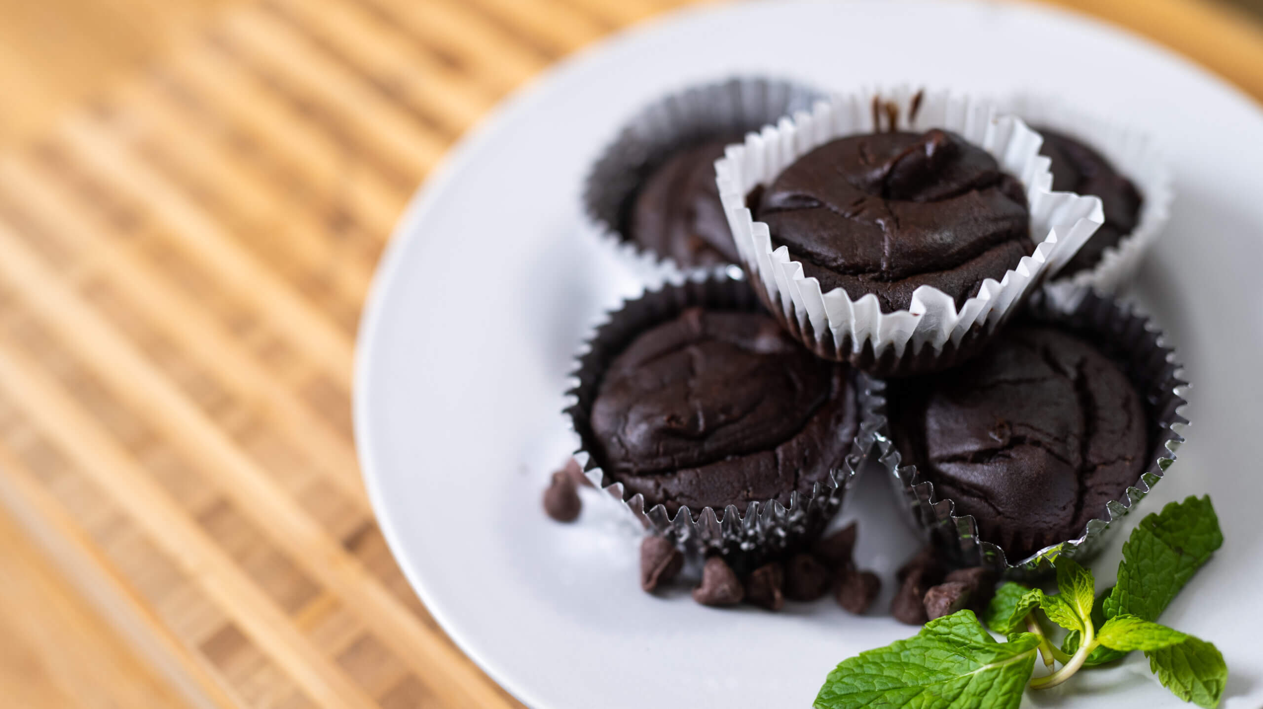 A plate of fudgy black bean brownies with crackly tops and chocolate chips on a warm-toned kitchen table with a glass of milk nearby
