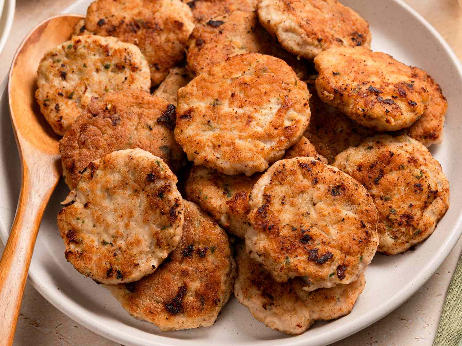 A plate of golden brown crispy chicken patties with a small bowl of dipping sauce on a wooden table in soft natural kitchen light