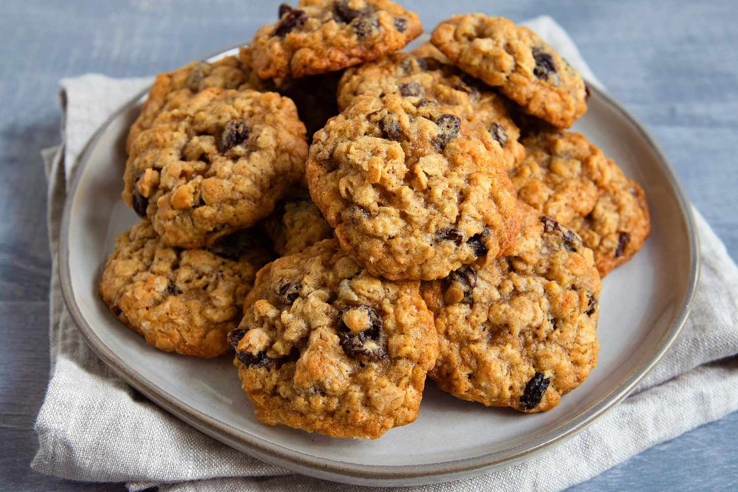 A plate of golden brown oatmeal cookies with visible rolled oats and lightly crisp edges on a wooden kitchen table in warm natural light