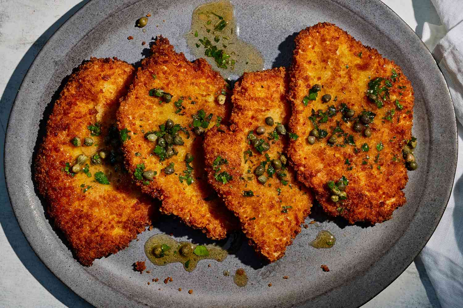 A plate of golden brown panko crusted chicken cutlets with crisp edges, served with lemon wedges on a simple dinner table
