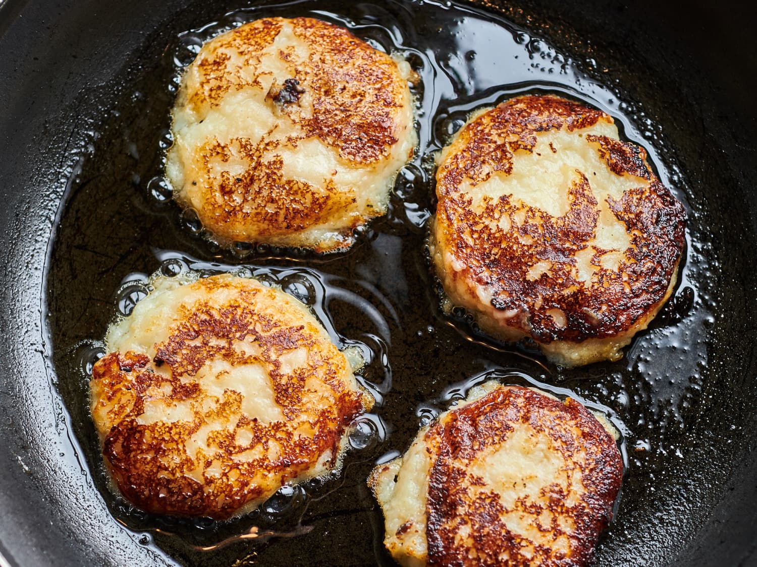 A plate of golden brown potato cakes with crisp edges and a dollop of sour cream, set on a simple dinner table with a fork and napkin