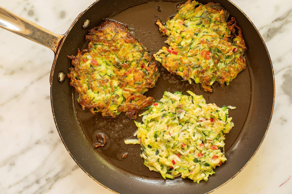 A plate of golden brown zucchini fritters with crisp edges stacked beside a small bowl of lemon yogurt sauce on a rustic kitchen table