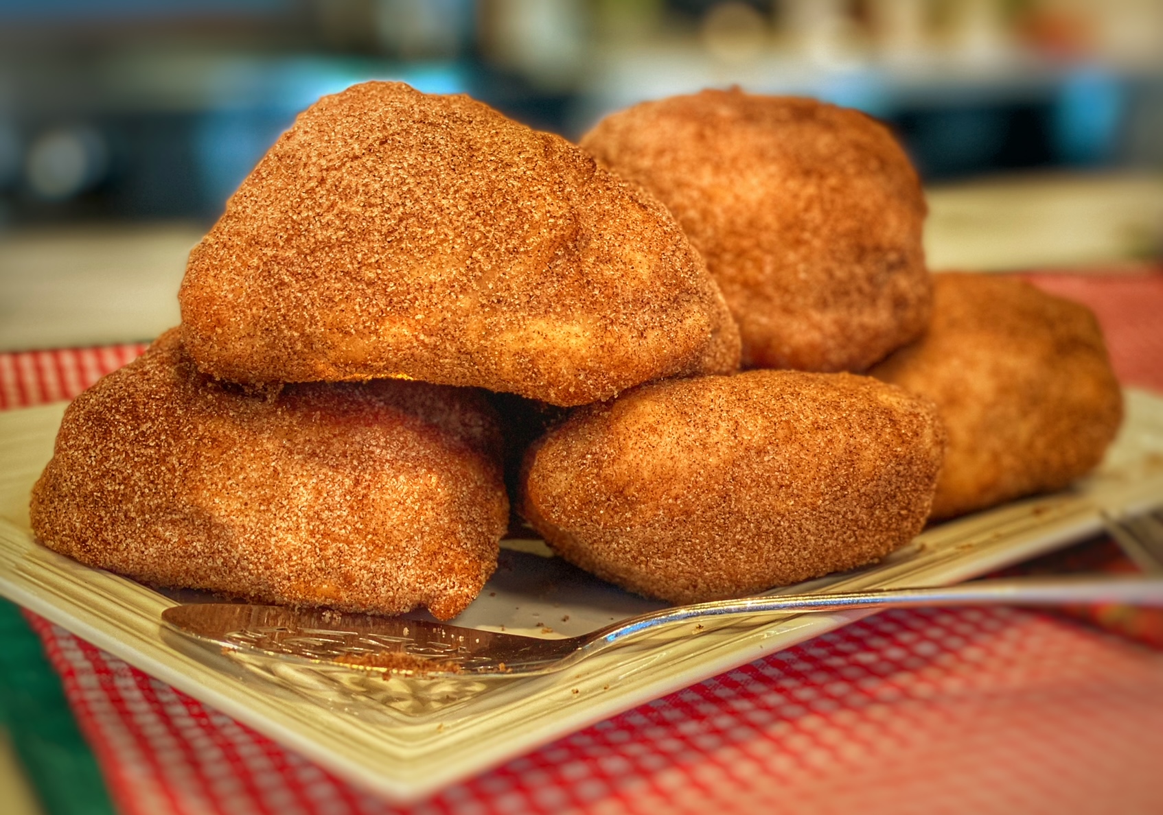 A plate of golden fried dough pieces coated in cinnamon sugar on a warm kitchen table with a small bowl of extra cinnamon sugar nearby, natural window light