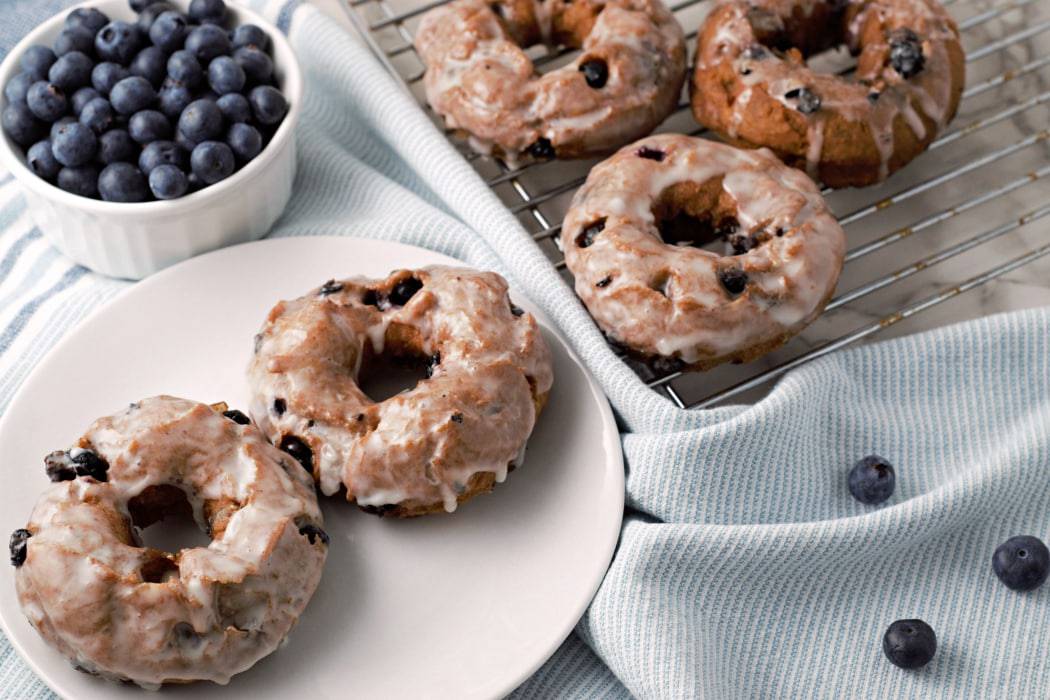 A plate of golden old-fashioned cake donuts with a shiny vanilla glaze on a wooden kitchen table in soft morning light