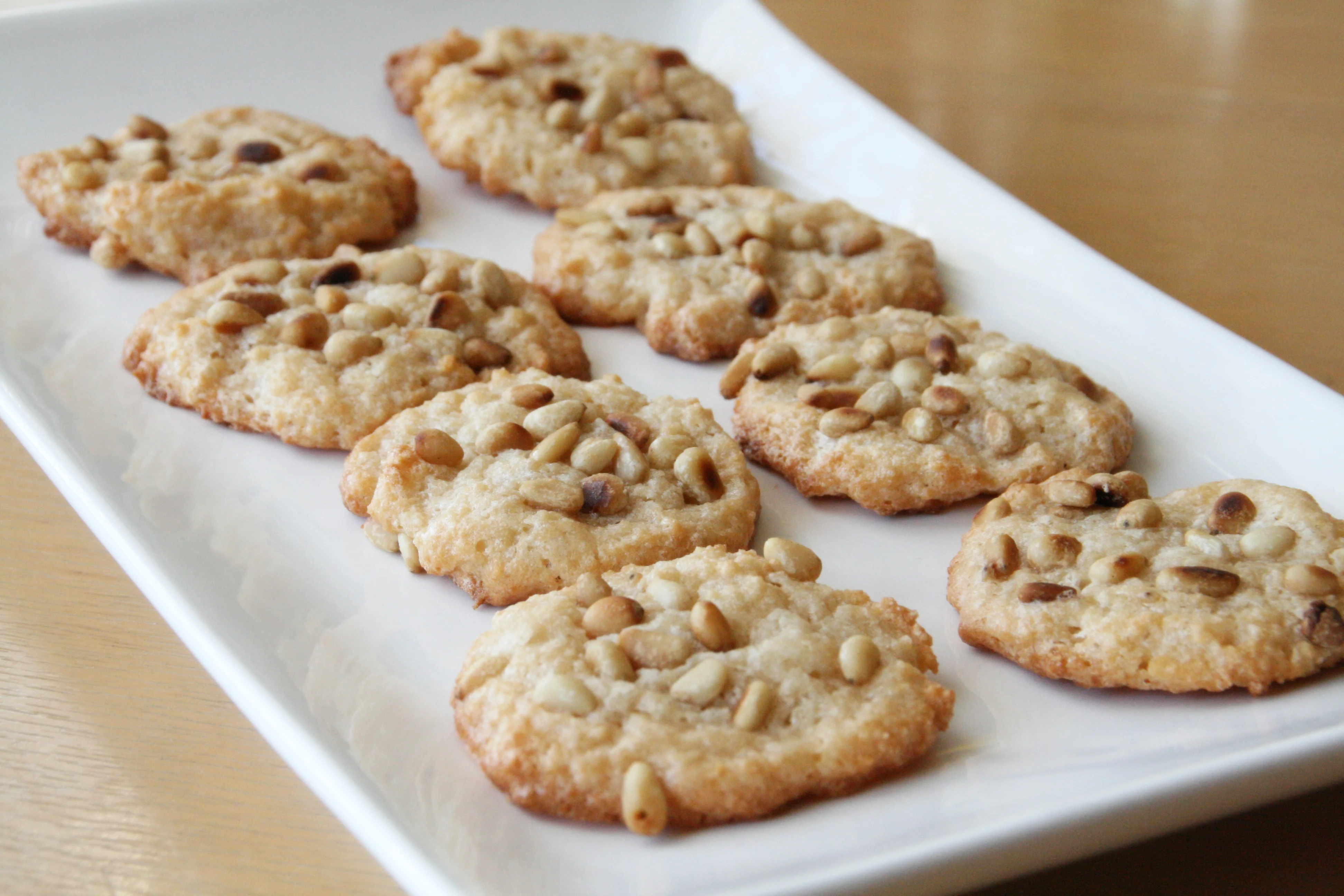 A plate of golden pignoli cookies covered in toasted pine nuts on a linen napkin on a bright kitchen table