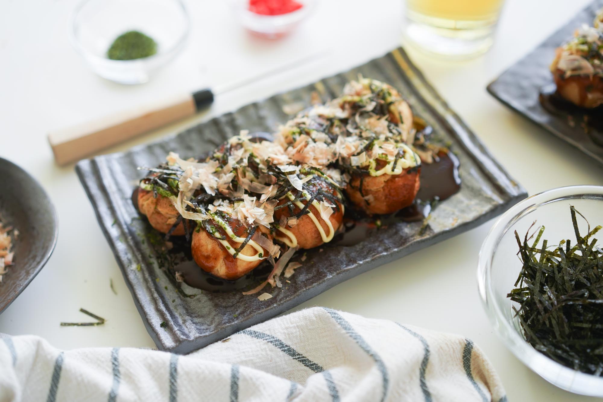 A plate of golden takoyaki topped with takoyaki sauce, Japanese mayo, bonito flakes, and aonori on a warm wooden table