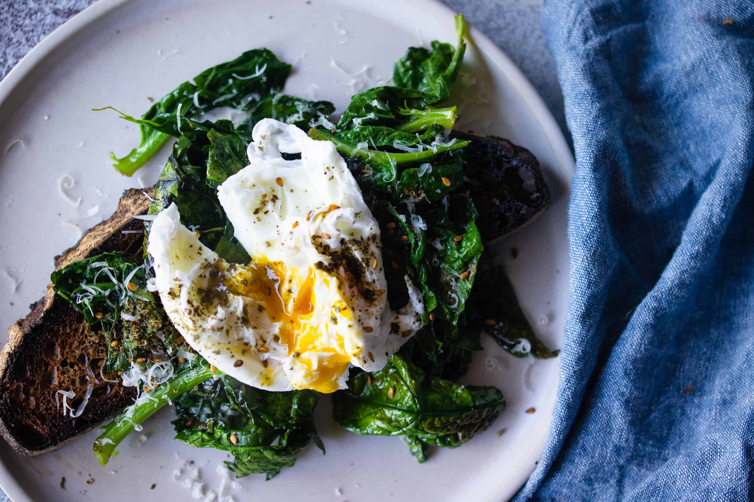 A plate of posh eggs, soft scrambled and glossy, piled on thick buttered toast and topped with chopped chives and flaky salt on a simple kitchen table