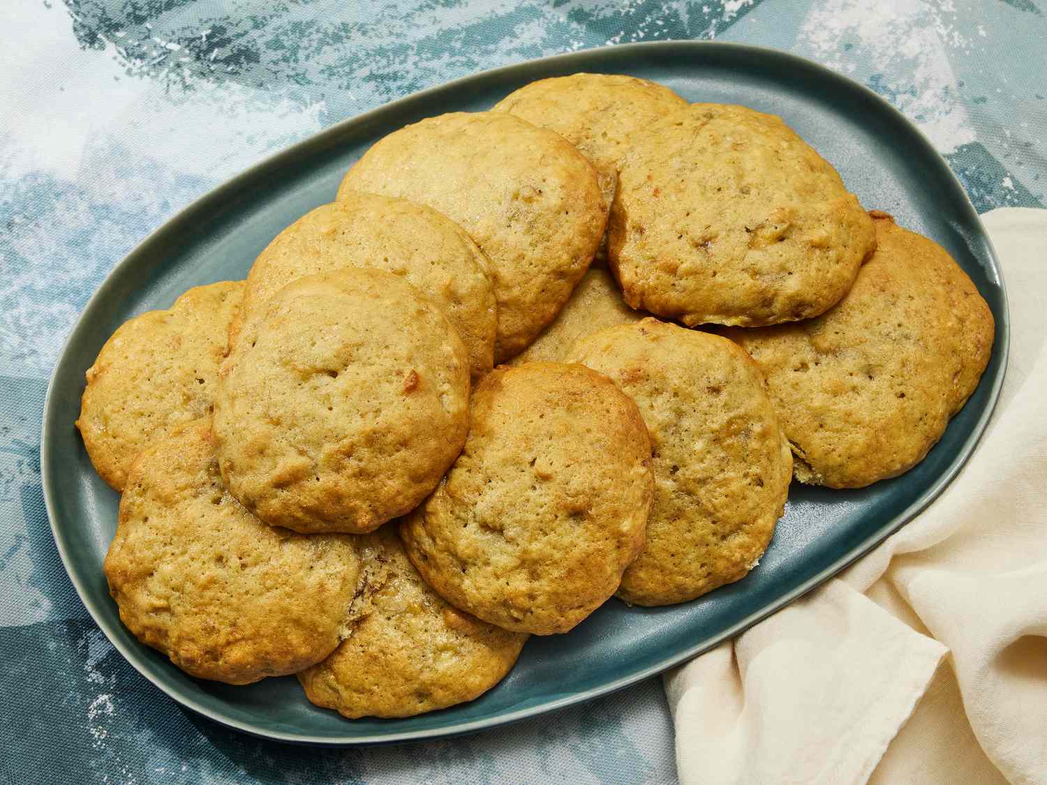 A plate of soft banana bread cookies with chocolate chips and lightly crisp edges on a wooden table, warm natural kitchen light