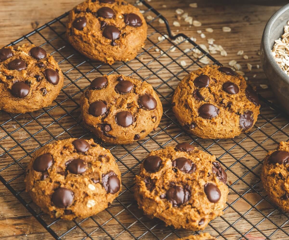 A plate of soft pumpkin chocolate chip cookies with melty chocolate chunks on a cozy kitchen table with a neutral linen napkin