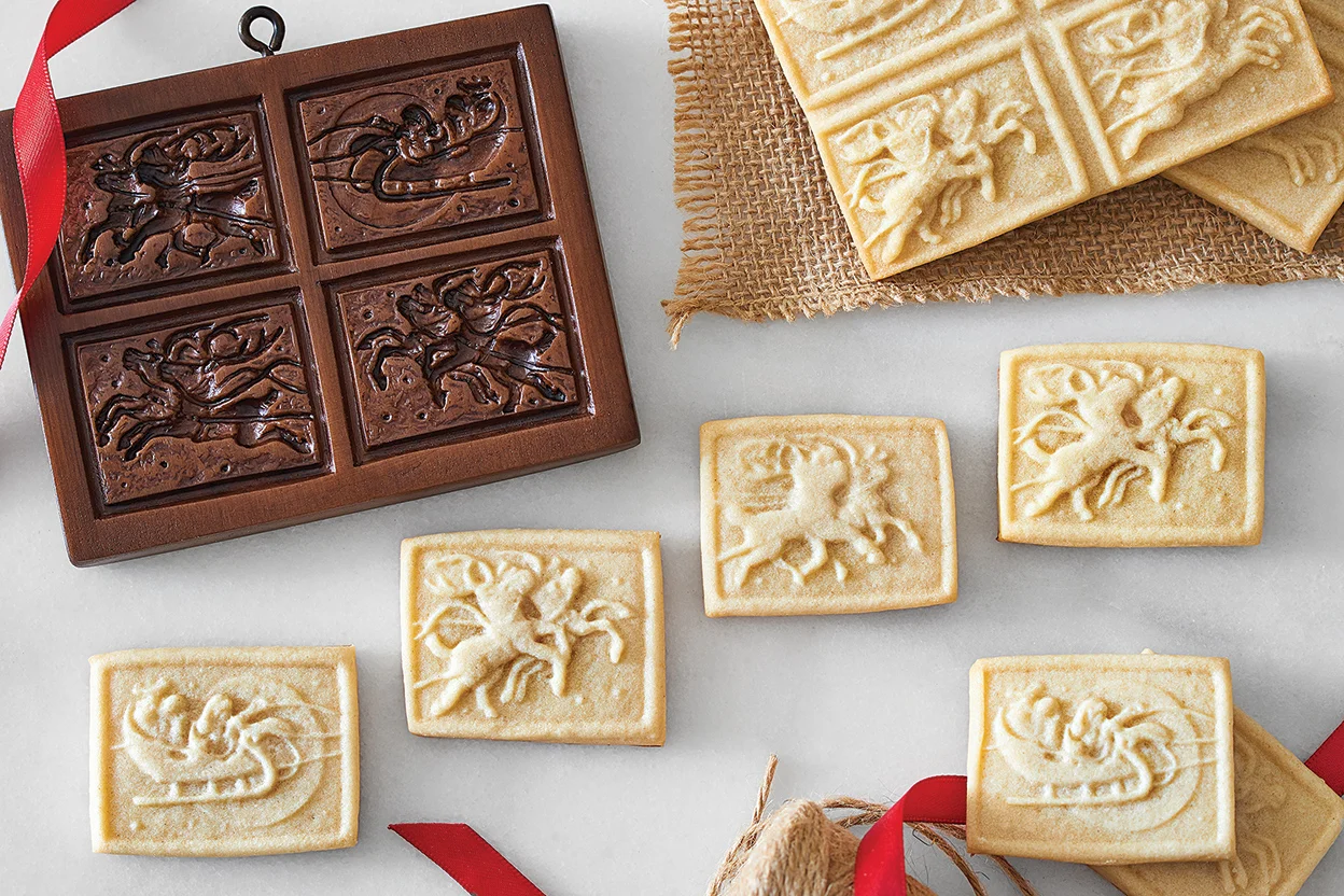 A plate of traditional Springerle cookies with crisp embossed designs and lightly golden bottoms on a simple wooden table setting