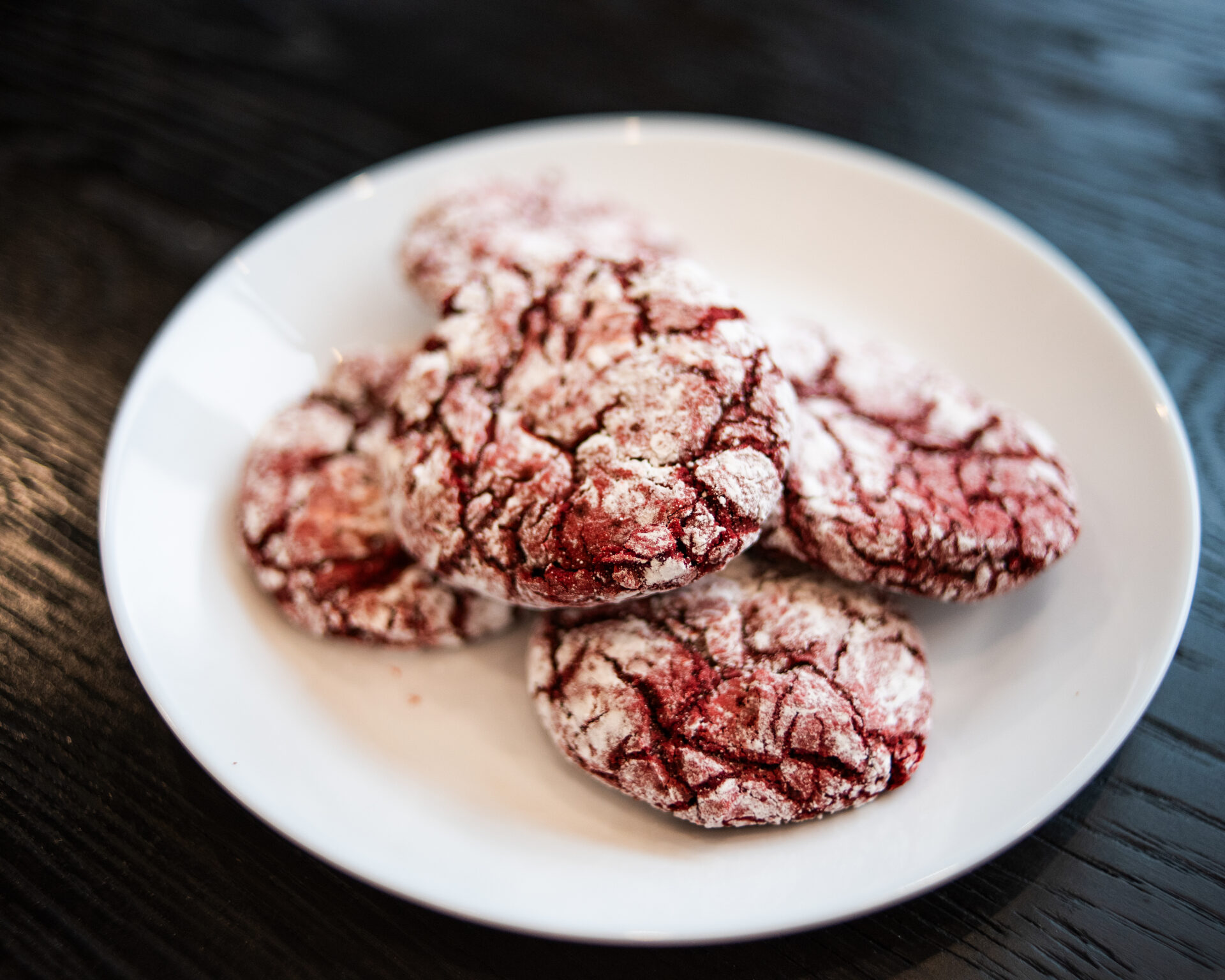 A plate of warm red velvet biscuits with a light cream cheese glaze drizzled over the tops on a wooden kitchen table in soft natural light