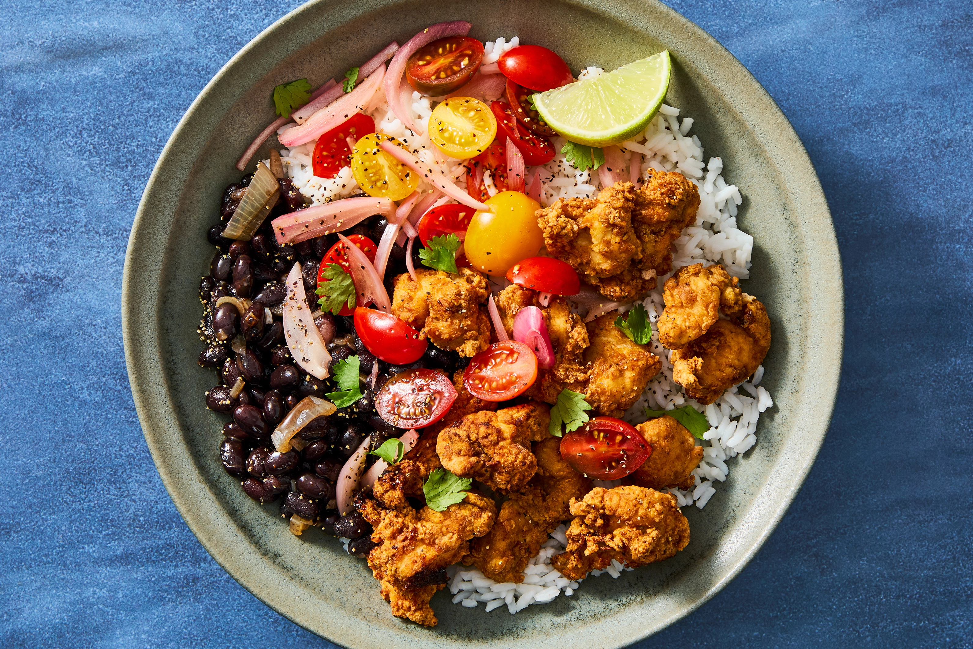 A plated Brazilian-inspired bowl with garlicky rice, black beans, golden seasoned chicken, and a fresh tomato lime salsa on a wooden table with soft natural light