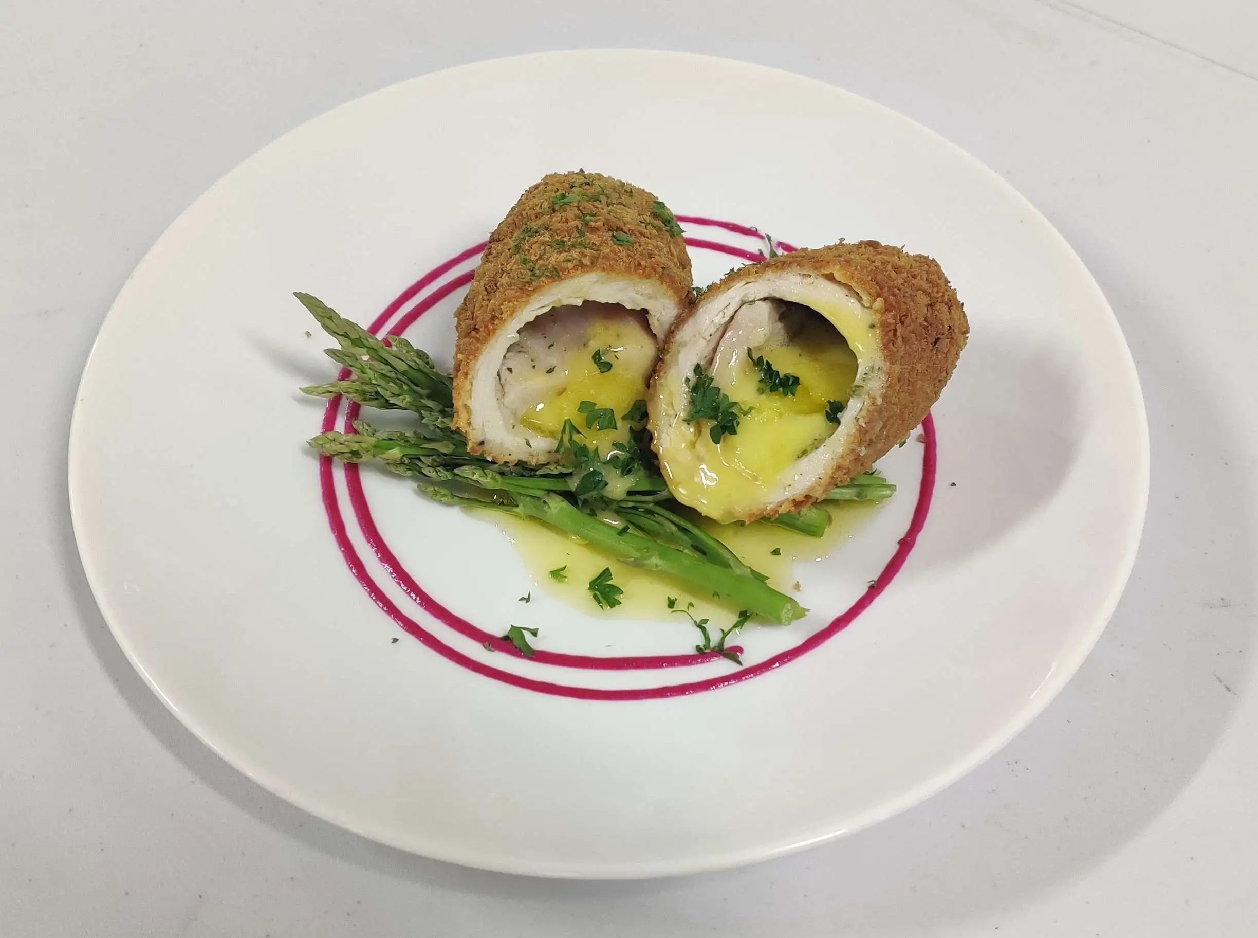 A plated Chicken Kiev cutlet sliced open with melted herb butter pooling on the plate, served with mashed potatoes on a white dinner plate in a warm home kitchen