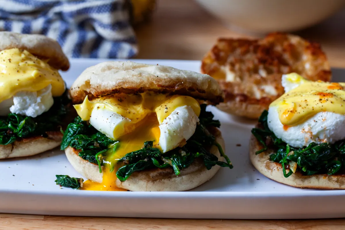 A plated Eggs Florentine with toasted English muffin halves topped with sautéed spinach, two poached eggs, and glossy hollandaise sauce, set on a bright kitchen table with soft morning light