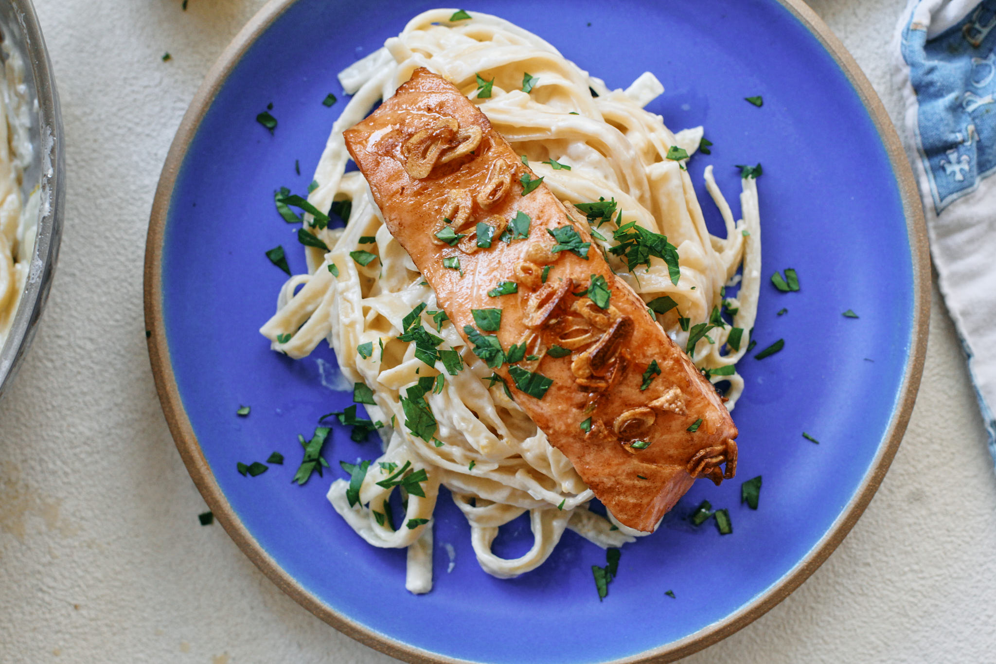 A plated bowl of creamy salmon pasta with visible flakes of salmon, wilted spinach, and lemon zest on top on a warm-toned dinner table