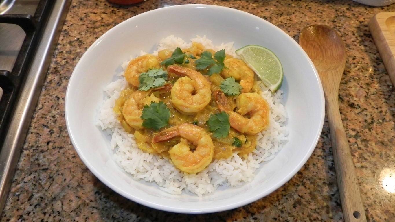 A plated bowl of shrimp curry over jasmine rice topped with fresh cilantro, with a lime wedge on the side