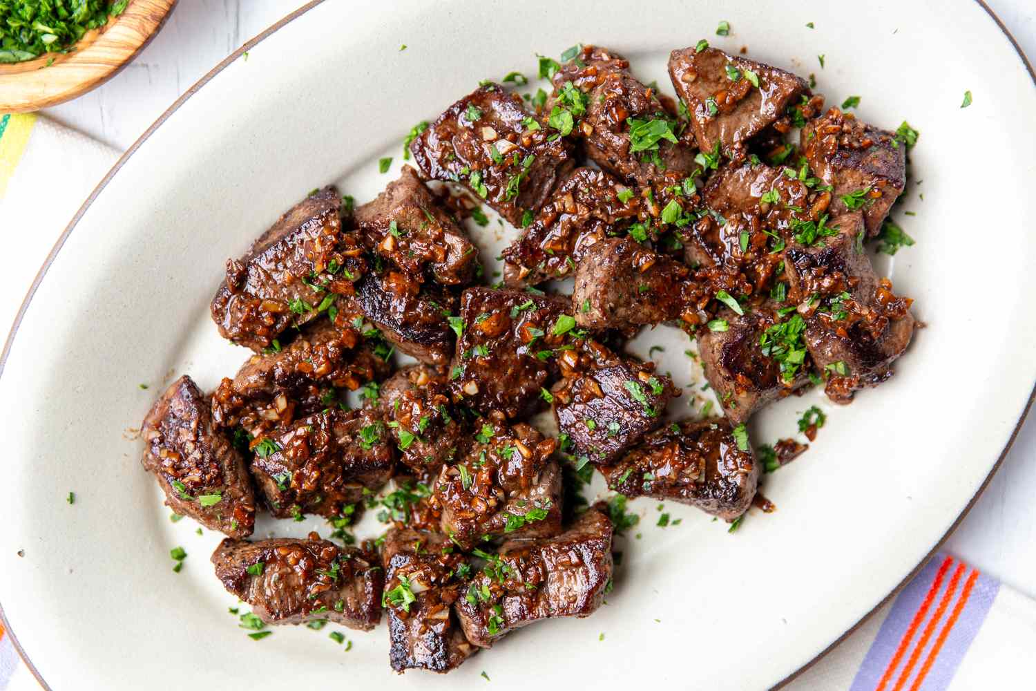 A plated garlic butter minute steak with crisp edges, glossy pan sauce, and chopped parsley on a white plate next to roasted potatoes on a wooden table