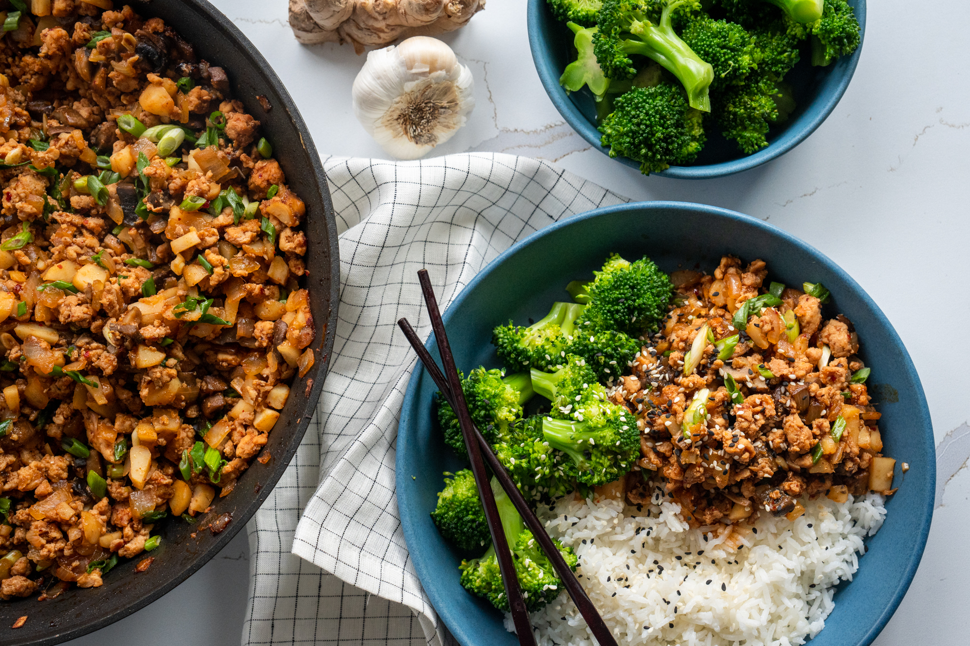 A plated healthy minced meat rice bowl with glossy ginger-soy ground chicken, cucumber ribbons, shredded carrots, and sesame seeds on a light wooden table
