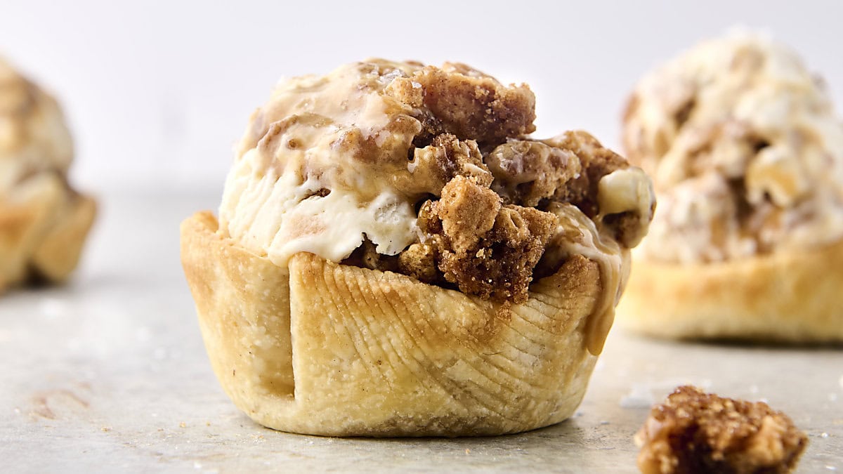 A plated mini apple pie topped with a scoop of vanilla ice cream, with cinnamon apple filling visible and a fork resting on the plate