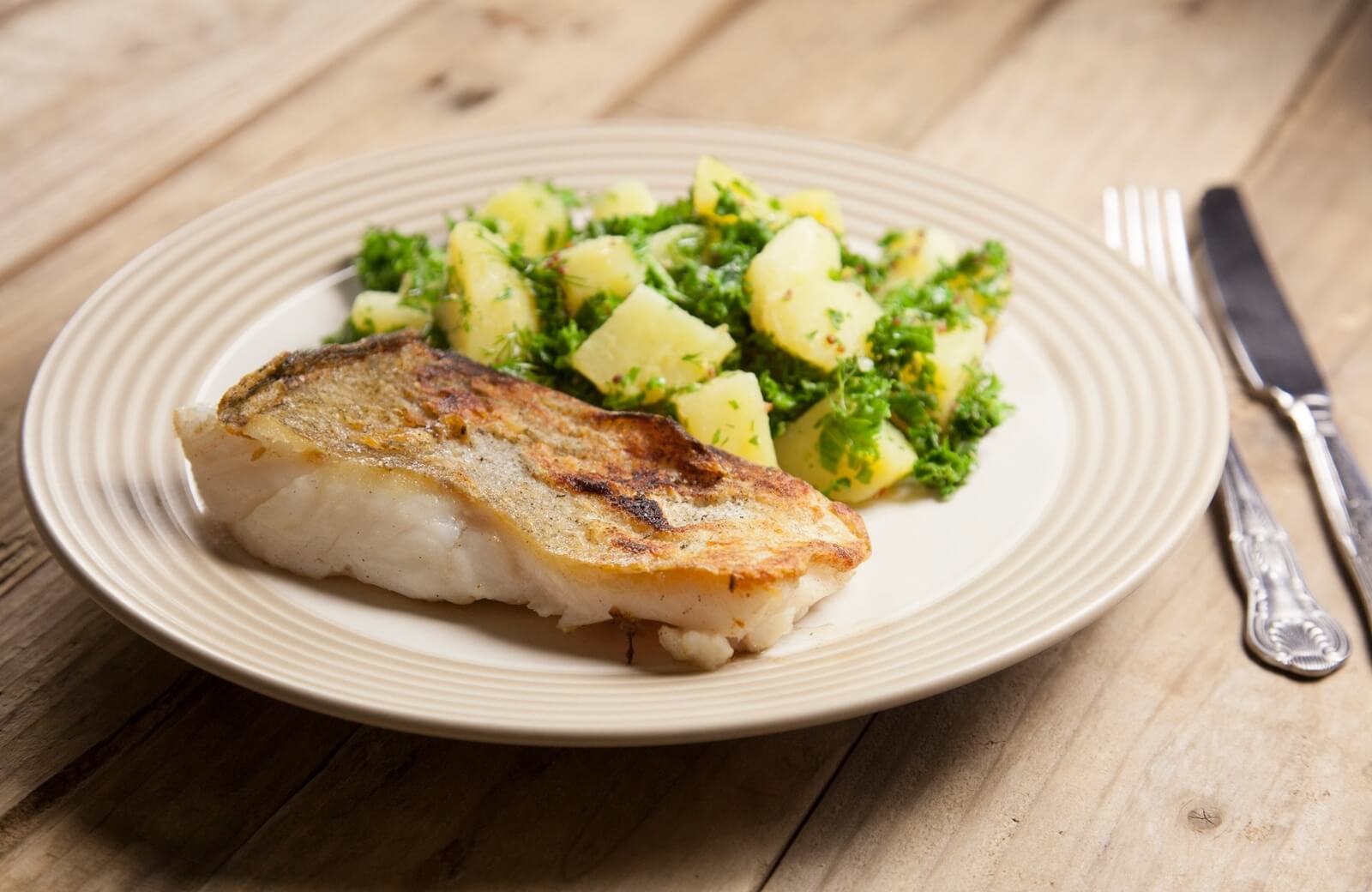 A plated pan seared pollock fillet with crisp golden edges, drizzled with lemon garlic butter sauce and sprinkled with chopped parsley, served on a white plate on a warm kitchen table