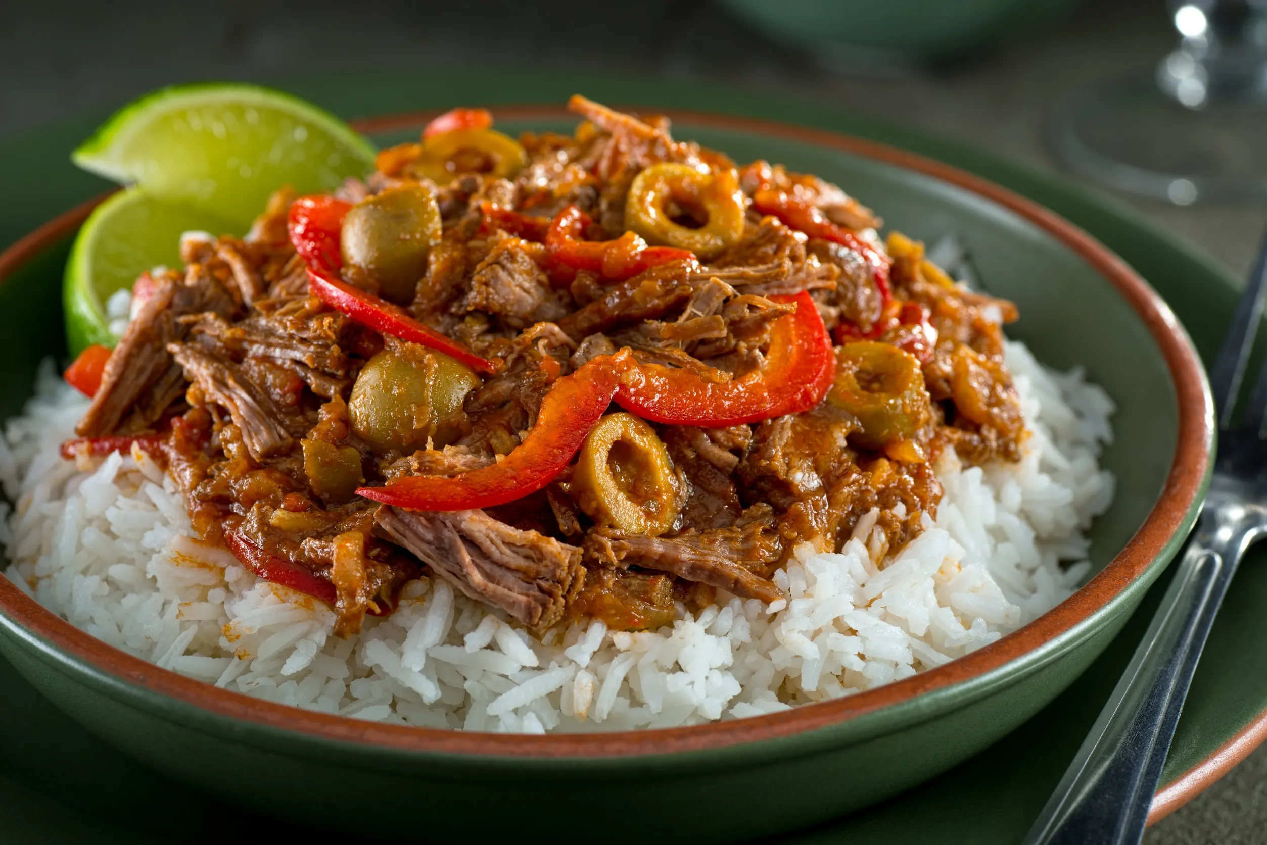 A plated serving of Filipino chicken asado with glossy soy-garlic sauce in a shallow bowl, steamed white rice on the side, and scallions sprinkled on top, warm kitchen lighting