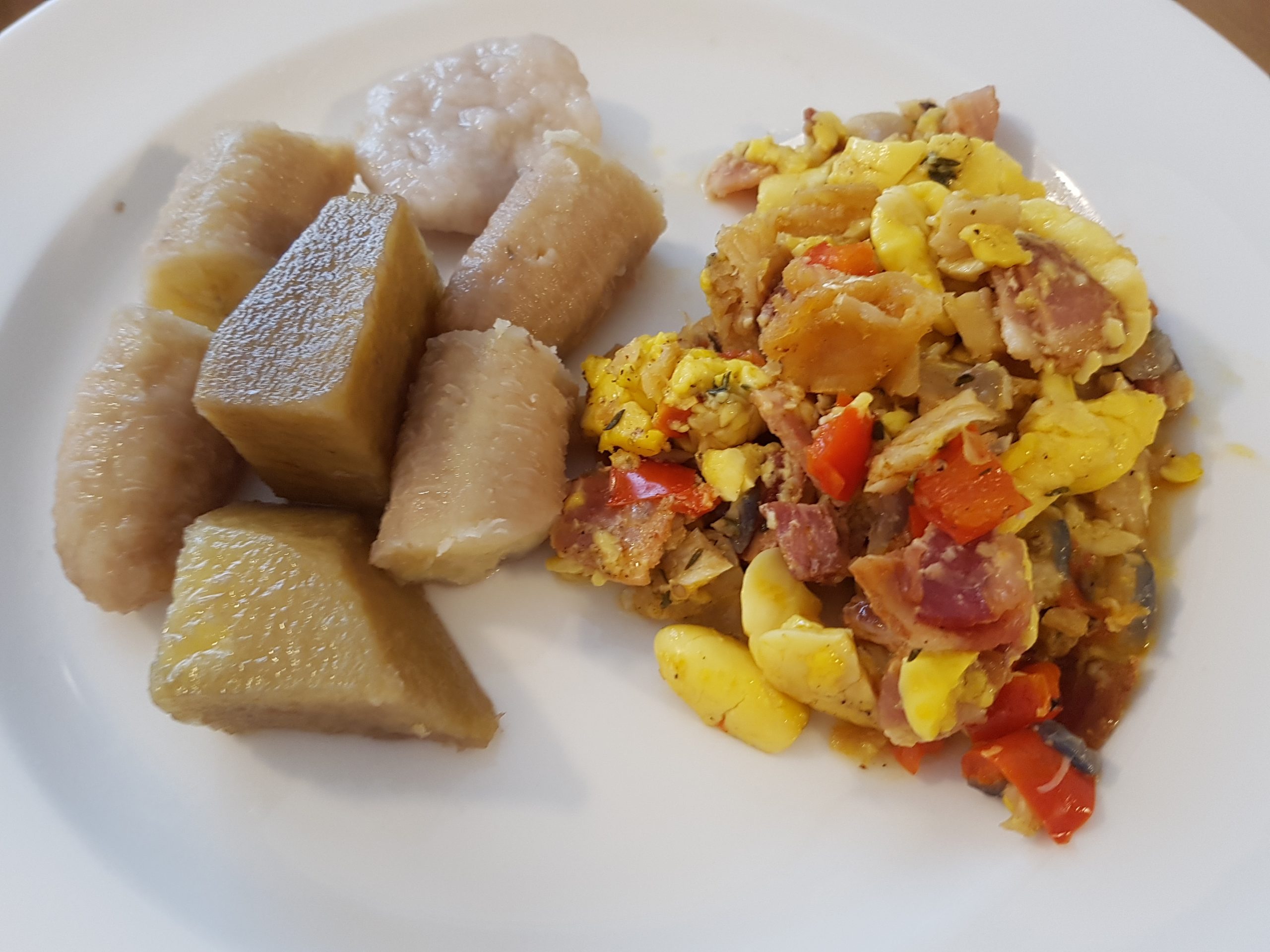 A plated serving of Jamaican ackee and saltfish with sautéed onions and bell peppers on a white plate, warm morning light on a wooden table
