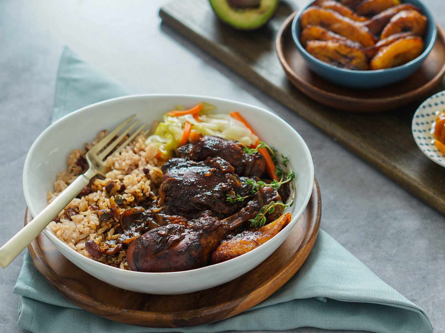 A plated serving of Jamaican brown stew chicken with glossy brown gravy, bell peppers, and thyme beside fluffy white rice on a simple dinner table