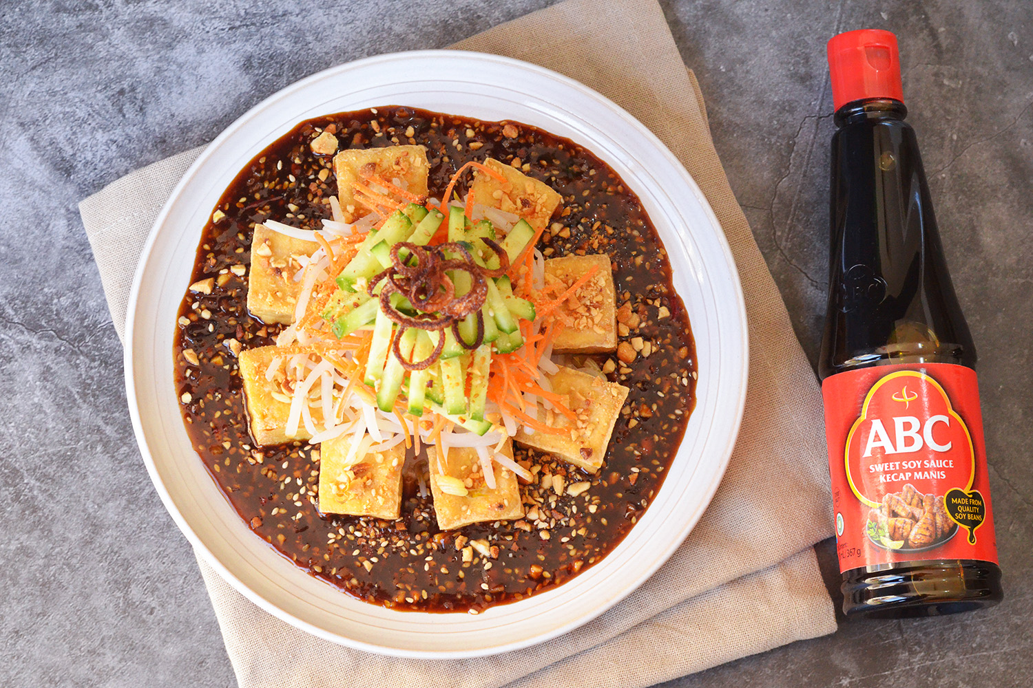 A plated serving of crispy Indonesian-style fried tofu (tahu goreng) drizzled with sweet soy lime sauce, garnished with sliced scallions and sesame seeds on a white plate